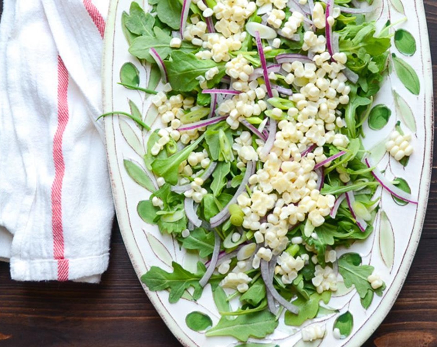 step 8 Arrange the Baby Arugula (115 g) on a large platter. Sprinkle the corn kernels over the arugula. Sprinkle on the red onion and scallions.