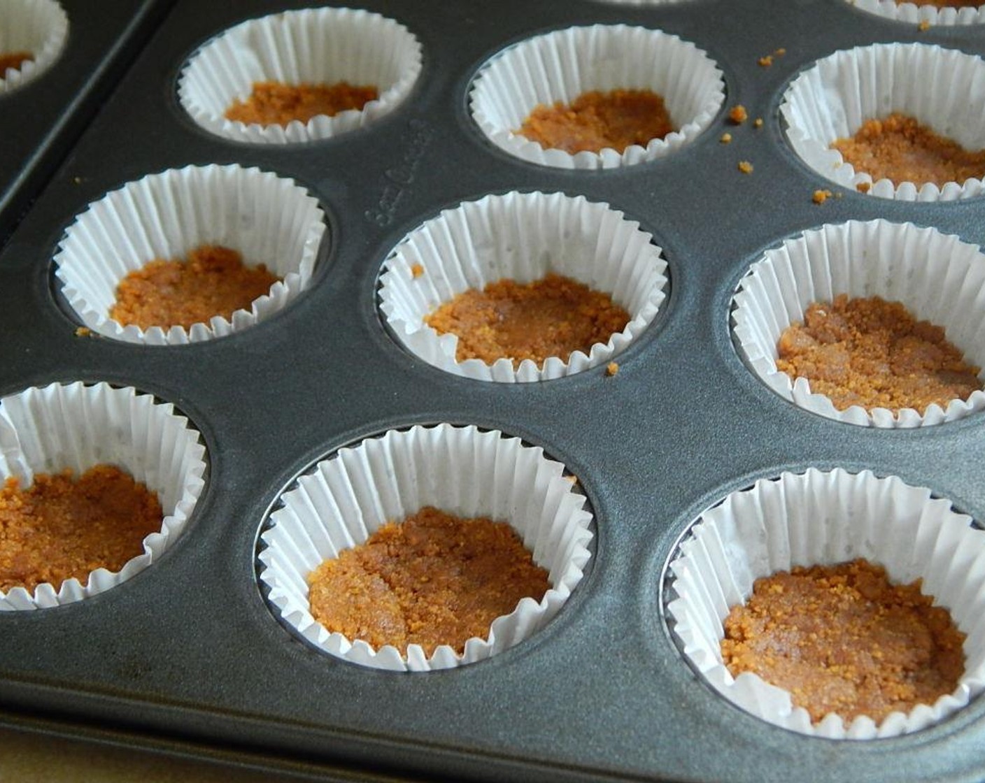 step 2 In a small bowl, mix the Graham Cracker Crumbs (1/2 cup), Light Margarine (1 1/2 Tbsp), and Ground Cinnamon (1/2 tsp) together. Divide over your 24 mini liners and pat down.