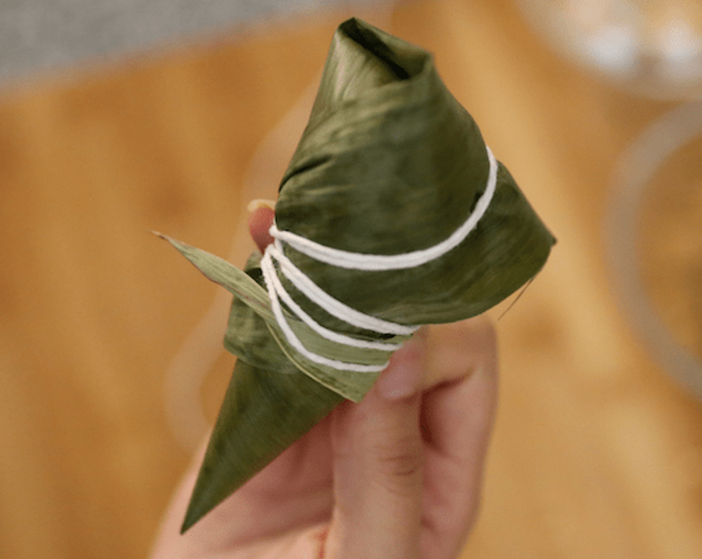 step 11 Turn down the palm leaf, wrap the dumplings with the cotton line with the palm leaf facing down on a flat surface, and wrap the dumplings with a cotton line.