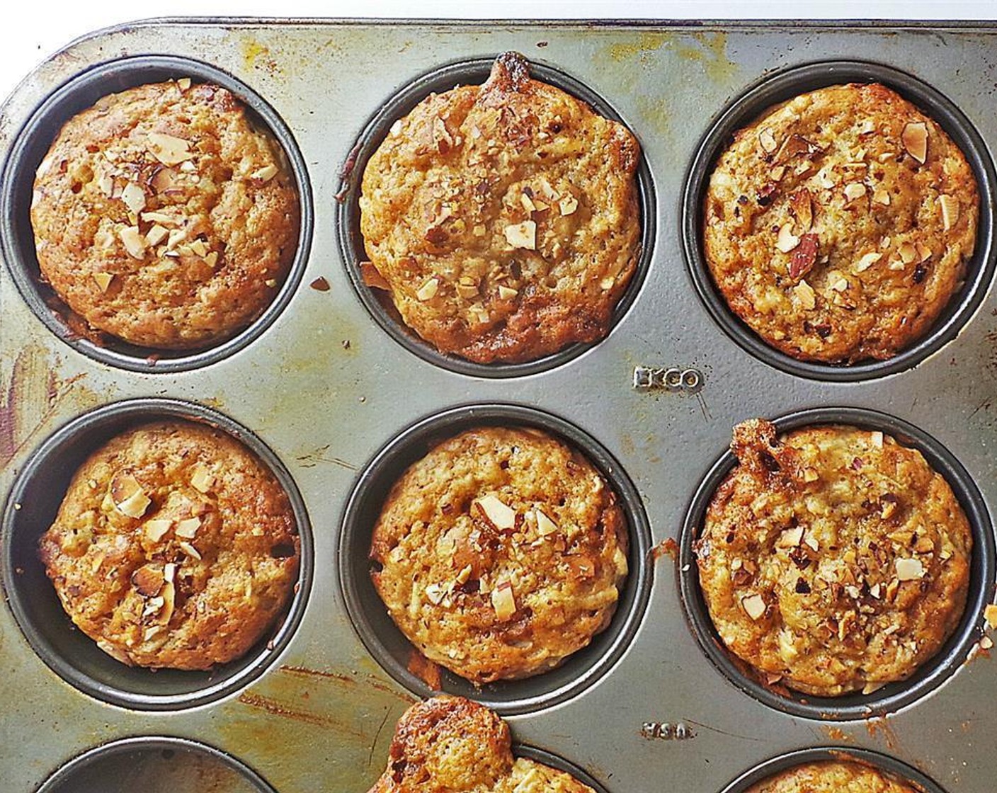 step 6 Grease a 12-tin muffin pan with Coconut Oil Cooking Spray (as needed) or line with muffin liners. Fill each tin 3/4 way full of batter. Evenly sprinkle the almonds on top of the muffins.