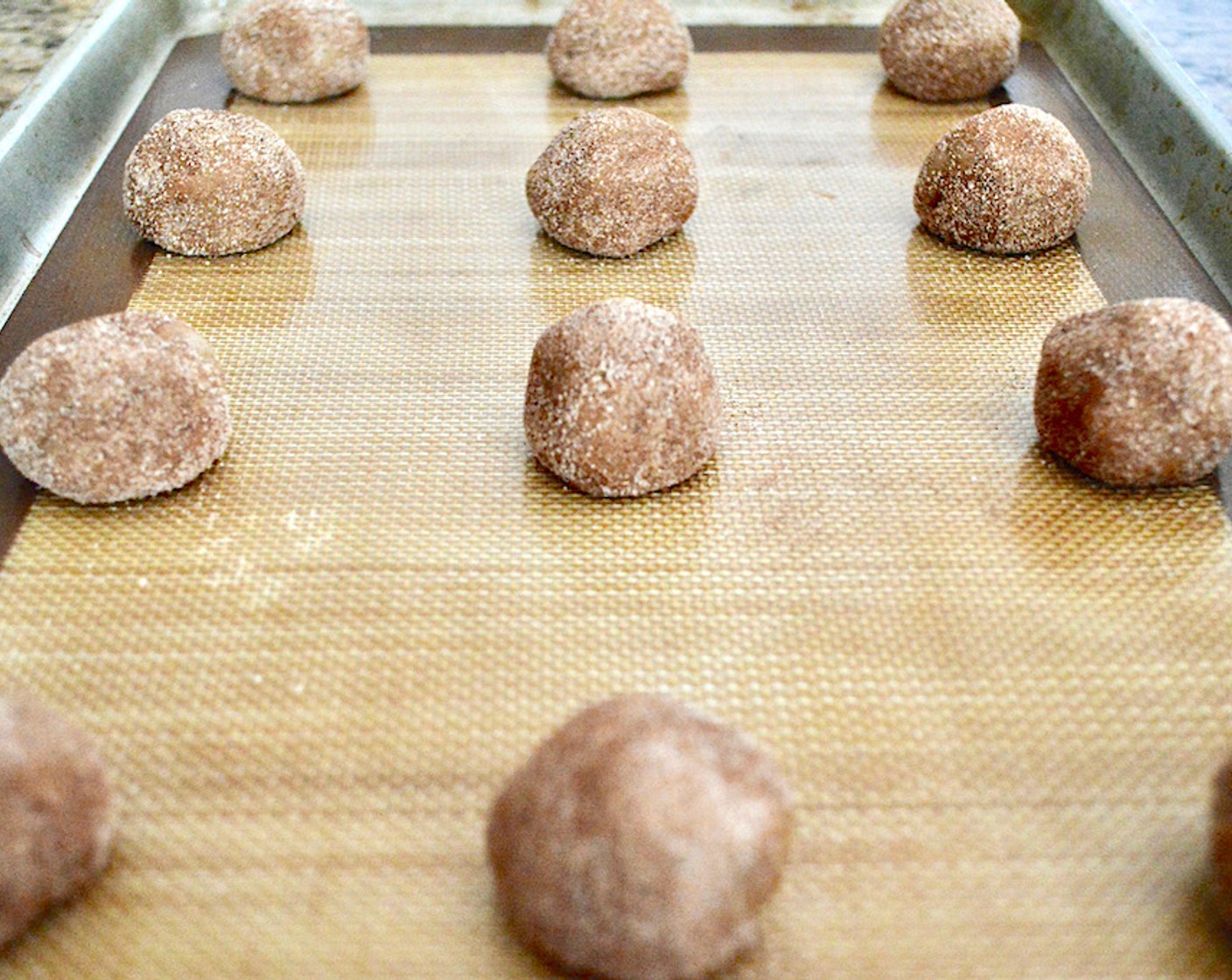 step 8 Use a cookie scoop to scoop a perfect mound of dough into your hand. Smooth it into a ball, then run it through the bowl of cinnamon and sugar to coat it. Repeat until you have a dozen coated balls of dough evenly spaced on each sheet tray.