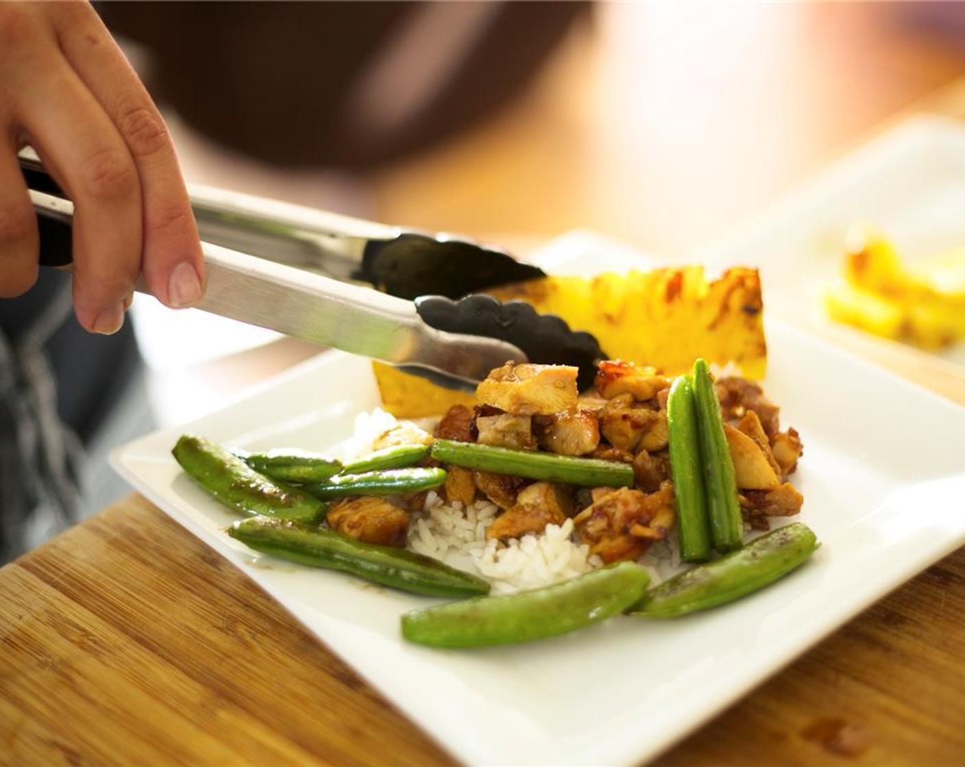 step 15 Divide rice between two plates. Place diced chicken over rice. Lay the peas over the rice next to the thicken. Place pineapple spear leaning against the back. Drizzle any extra sauce over the chicken.