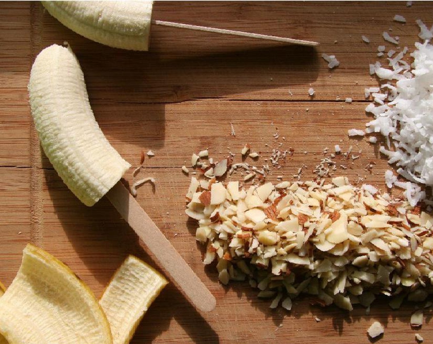 step 2 Cut Bananas (3) in half and pop them onto a popsicle stick. Dip the banana halves into the melted chocolate and place them onto a cookie sheet. Sprinkle with Sliced Almonds (1 handful) and Unsweetened Shredded Coconut (to taste).