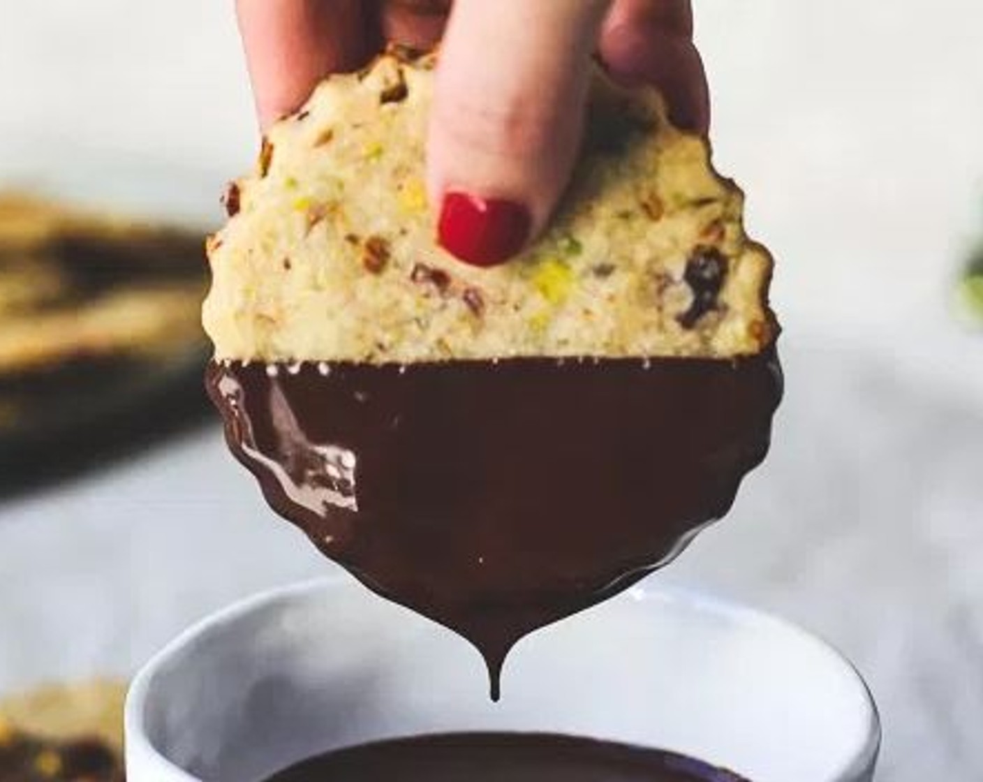 step 9 Remove cookies from the freezer and dip half the cookie into the melted chocolate. Set on clean parchment paper and sprinkle with extra dried cherries and pistachios.