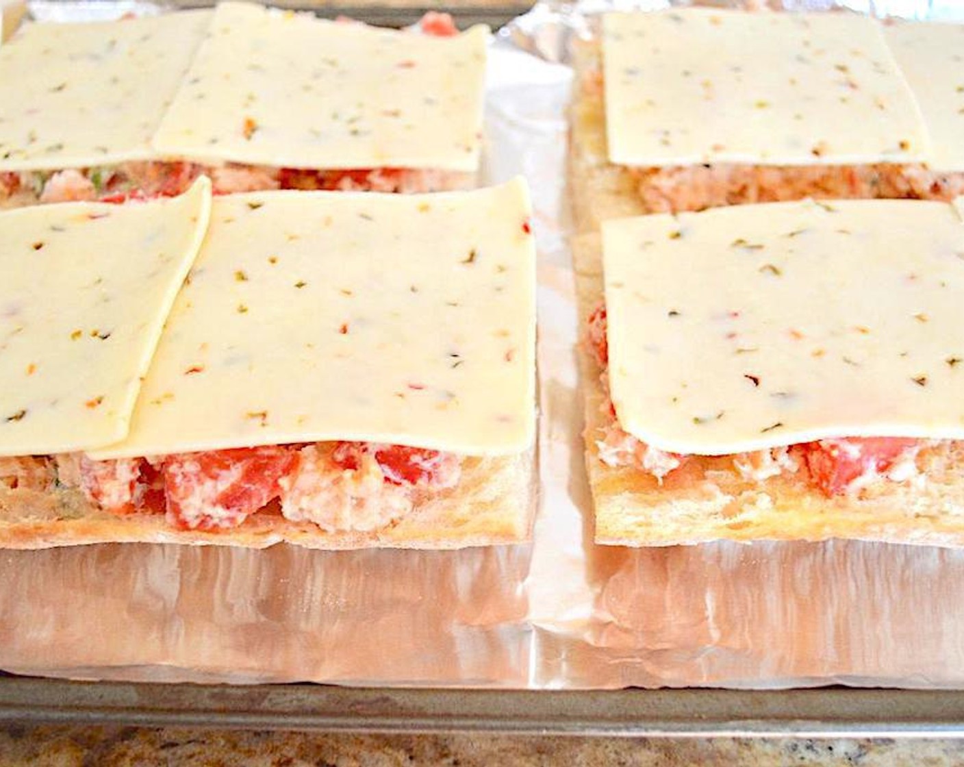 step 6 When the garlic bread is done, divide the crab mixture evenly among the 4 pieces of ciabatta and spread it out in an even layer. Top each piece with two slices of Pepper Jack Cheese (8 slices) and return the sheet pan to the oven for another 10 minutes. The cheese should get bubbly and the mixture cooked through.