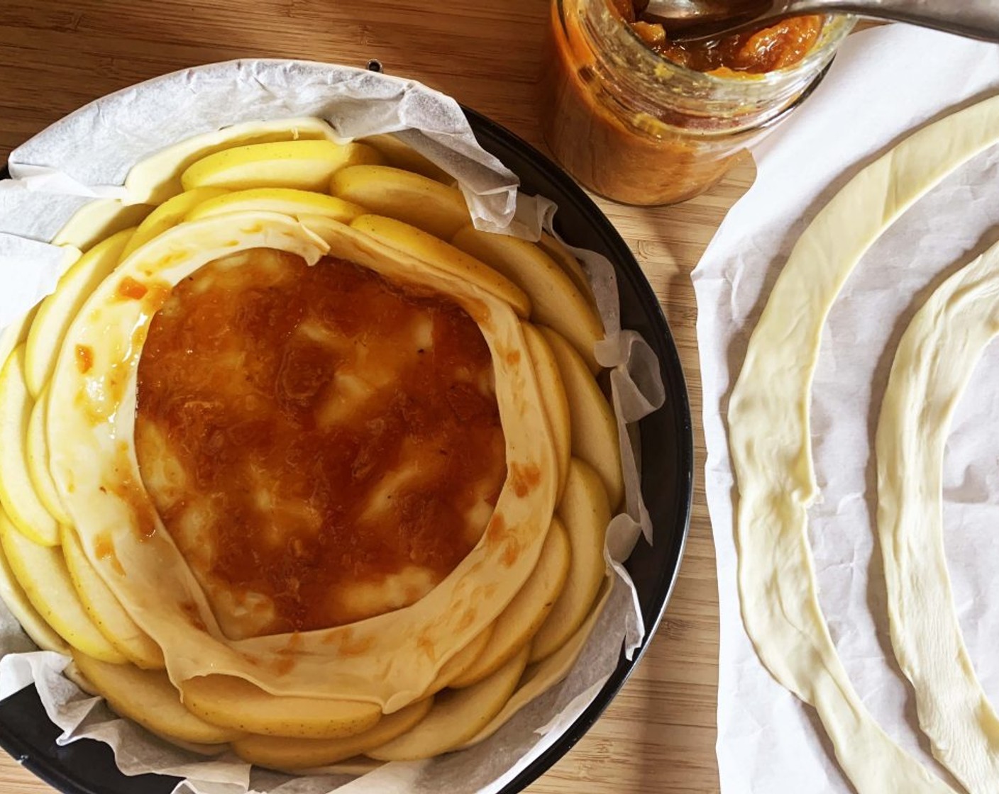 step 5 Brush the bottom of the cake with a few tablespoons of Orange Jam (2 Tbsp). Start laying around the edges 2 rounds of sliced apples, then make one round with the puff pastry strips. Brush with more jam. Repeat until you reach the center.