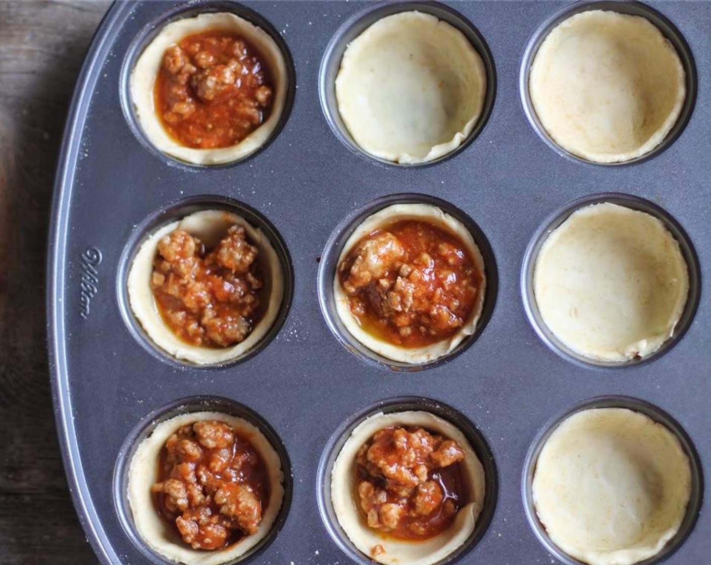 step 4 Place the larger circles of dough into each muffin tin, pressing to form little pies neatly in each tin. Spoon 2 to 3 tablespoons of meat and sauce into each pie.
