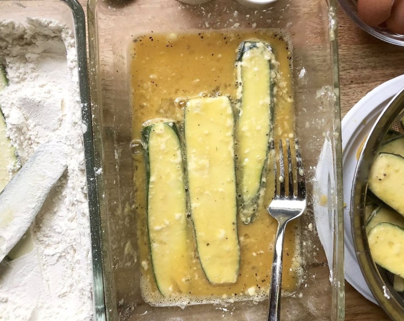 step 3 Tumble 5 or 6 zucchini strips at a time in the flour, coating them well on both sides. Shake off loose flour and slide the strips in the beaten eggs. Turn and separate the strips with a fork so they're all covered with batter; pick them up one at a time and let excess egg drip back into the bowl; then lay them in the colander.