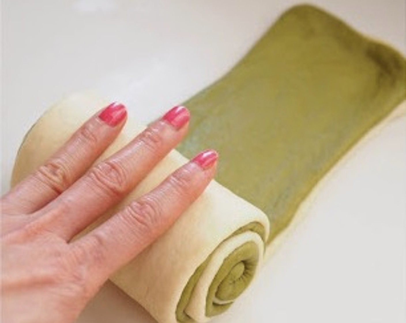 step 8 Spray water on the plain dough and place the matcha dough over the plain dough. Press with your palm to make sure both layers stick together. Spray some water on the matcha dough and roll it up tightly, starting from the shorter side until a log is formed. Pinch to seal the seams.