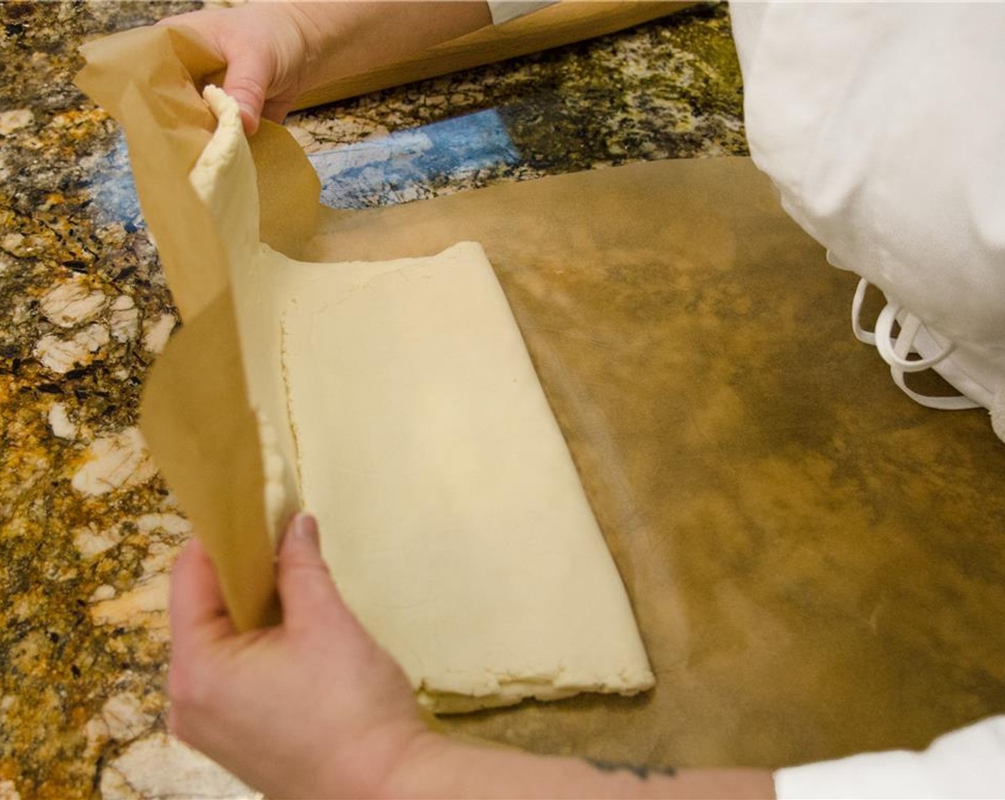 step 11 Remove the top layer of plastic wrap or parchment paper. Using the bottom layer of plastic wrap or parchment to assist in moving the dough, fold the bottom third of the dough up towards the center.