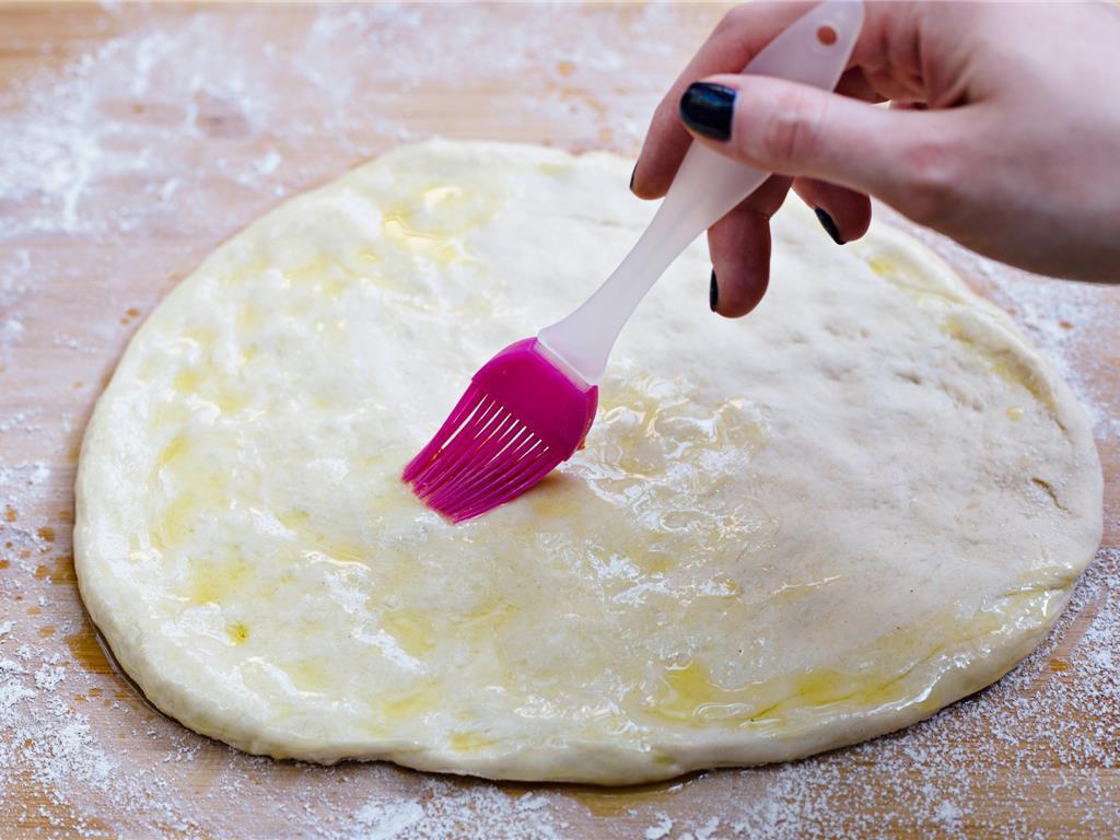 brushing pizza crust with olive oil for enhanced taste