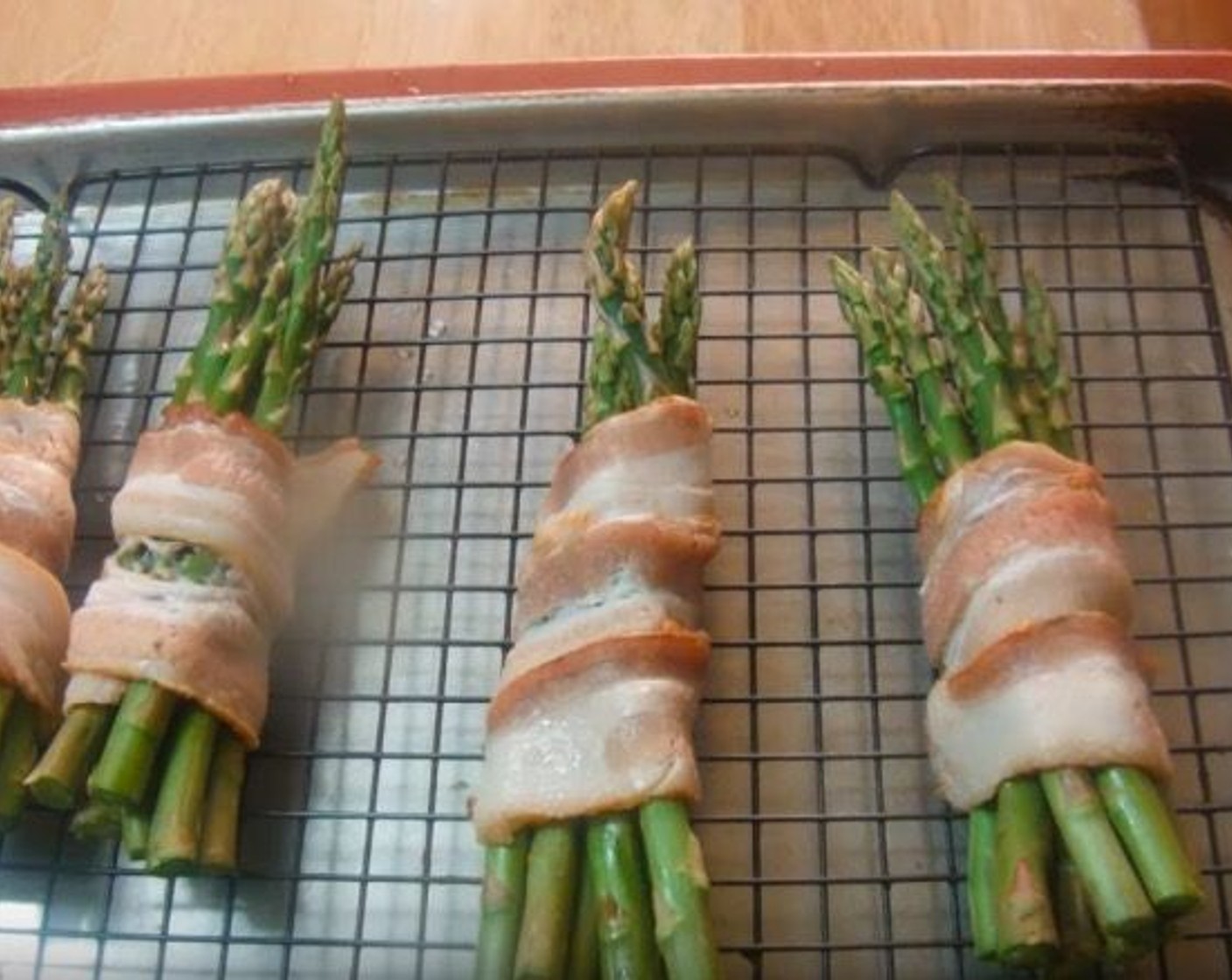 step 2 Divide Asparagus (1 bunch) into four smaller bunches. Wrap each with Bacon (to taste). Place on a wire rack in a baking pan.
