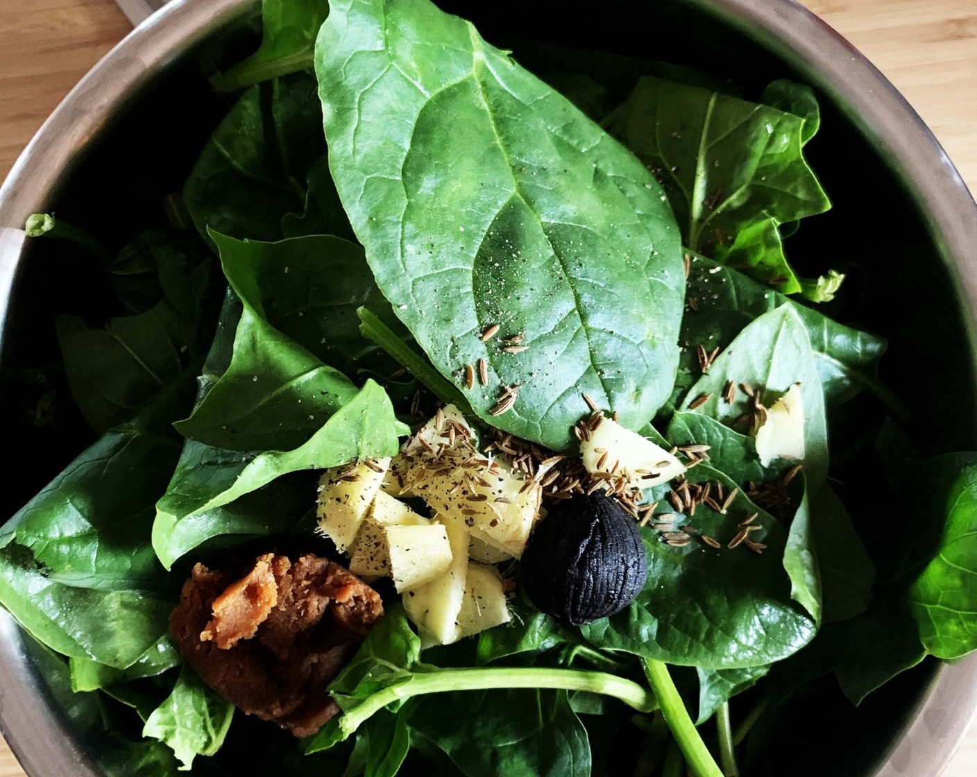 step 1 Place Fresh Spinach (14 oz), Black Garlic (1/2 head), Fresh Ginger (1 piece), Miso Paste (1 Tbsp), Cumin Seeds (to taste), and Ground Black Pepper (to taste) in a large saucepan, add Water (1/2 cup) and bring to a simmer.