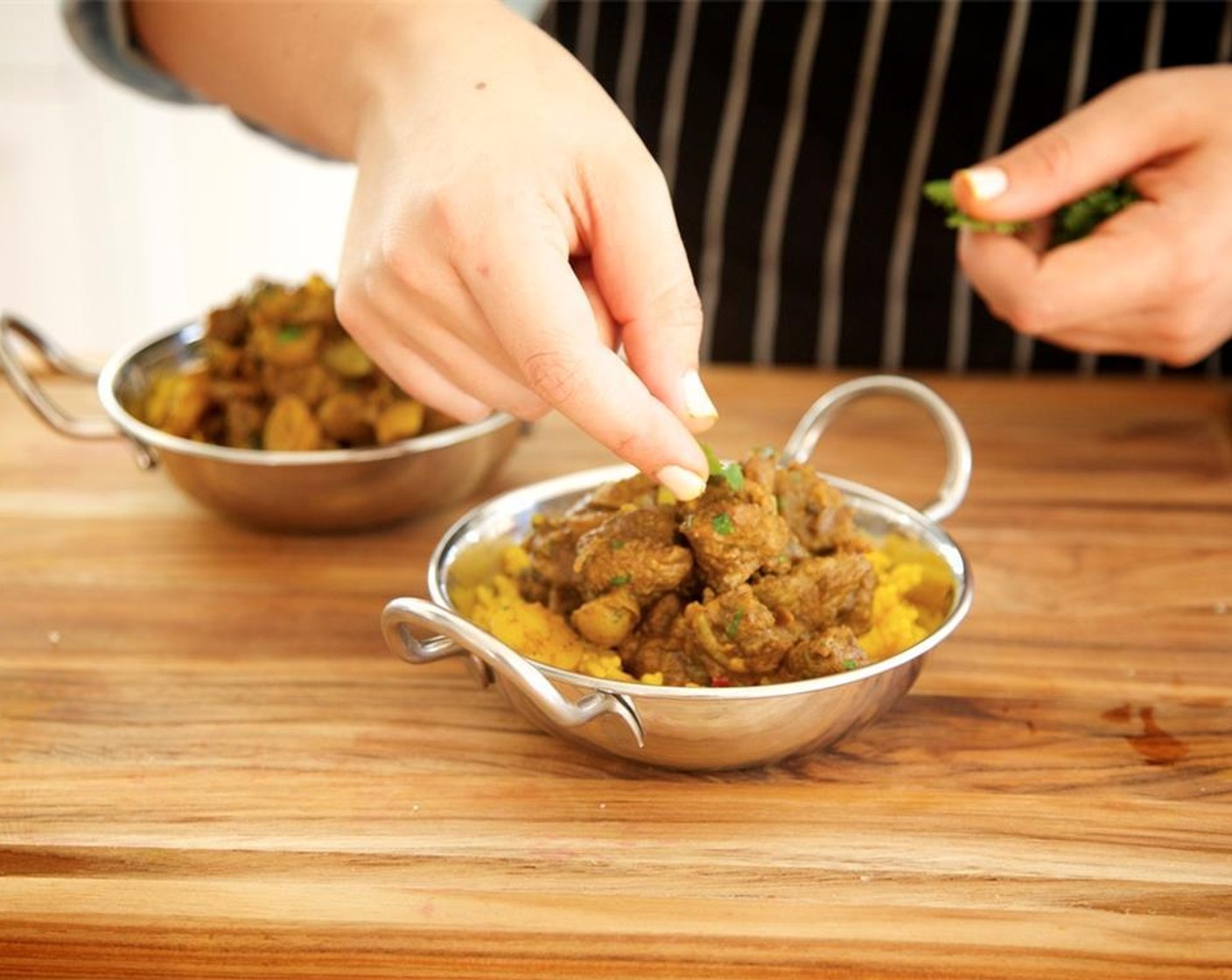 step 14 Place a scoop of turmeric rice into the center of two bowls. Top with the lamb curry and garnish with cilantro leaves. Serve the raita and folded naan on the side.