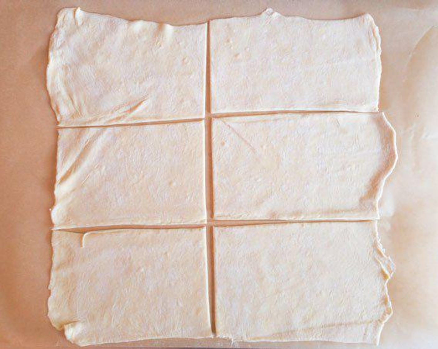 step 6 Put parchment paper on top of pizza pan. Directly on parchment paper, roll out the puff pastry as much as possible. Make into about a 12-inch square. With a pizza wheel, cut the dough to make 6 equal pieces, which allows for more even baking with the thick sweet potato layer.