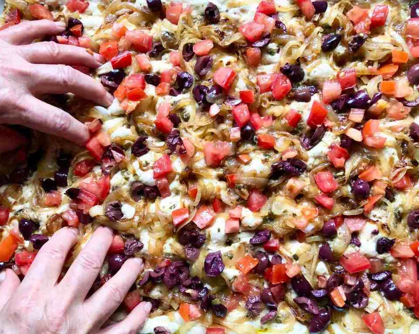 step 12 Spread the anchovy puree over the surface of the dough, followed by the sautéed onions then the Kalamata Olives (1/2 cup) and Diced Tomatoes (1 cup). Use all 10 fingers again to dimple the dough and gently stretch it.