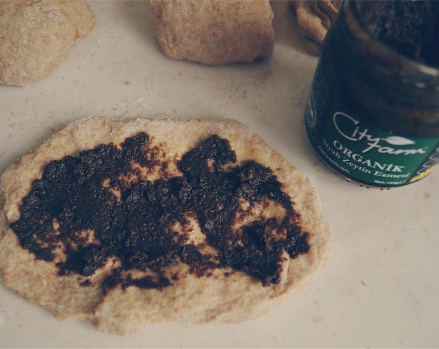 step 5 To shape the dough, use your hands to stretch each dough piece into an oval shape, and spread some Black Olive Tapenade (1/2 cup) evenly onto dough, leaving about a 1/4 inch margin around the sides.