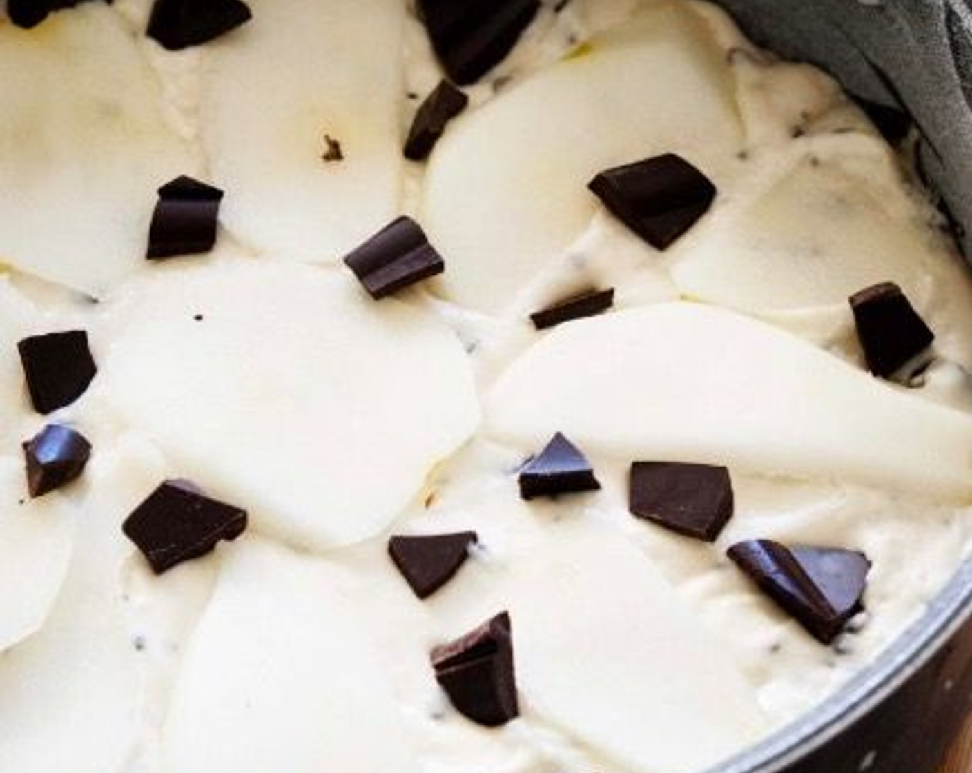 step 4 Using additional coconut oil, grease an 8-inch round baking pan and lightly dust it with flour. Pour the batter into the cake pan. Peel the other Pear (1) and slice into thin wedges. Place them on top of the cake, then add some more chocolate chips.