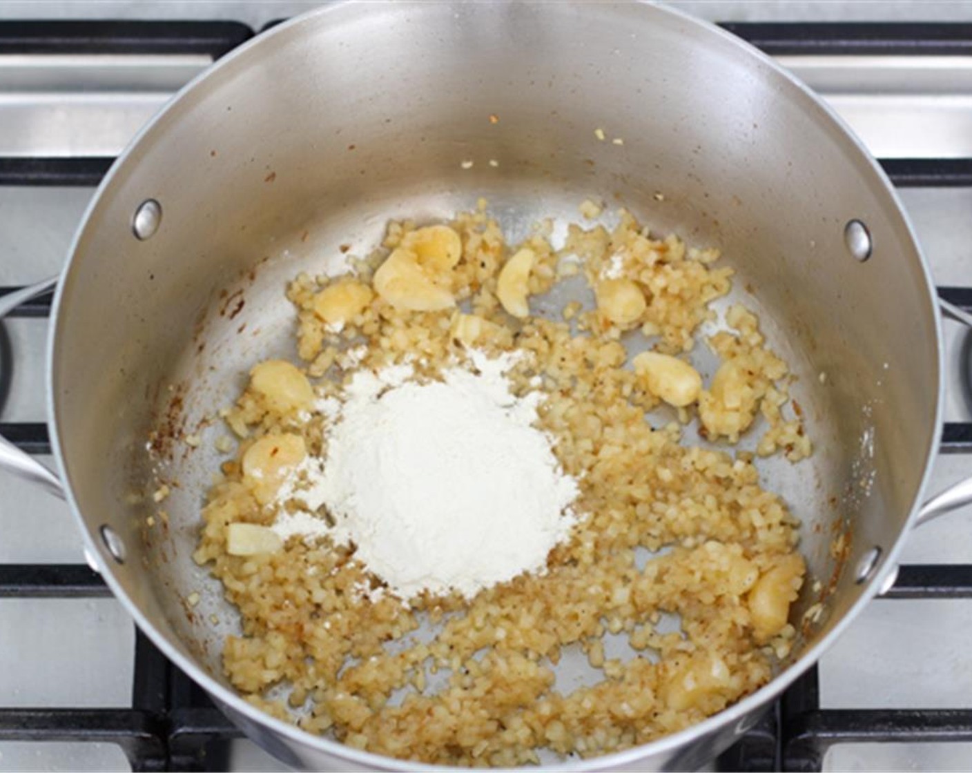 step 7 Add all the peeled cloves of Garlic (1 bulb) and then the All-Purpose Flour (1/4 cup). Mix the flour into the onions and oil until incorporated.