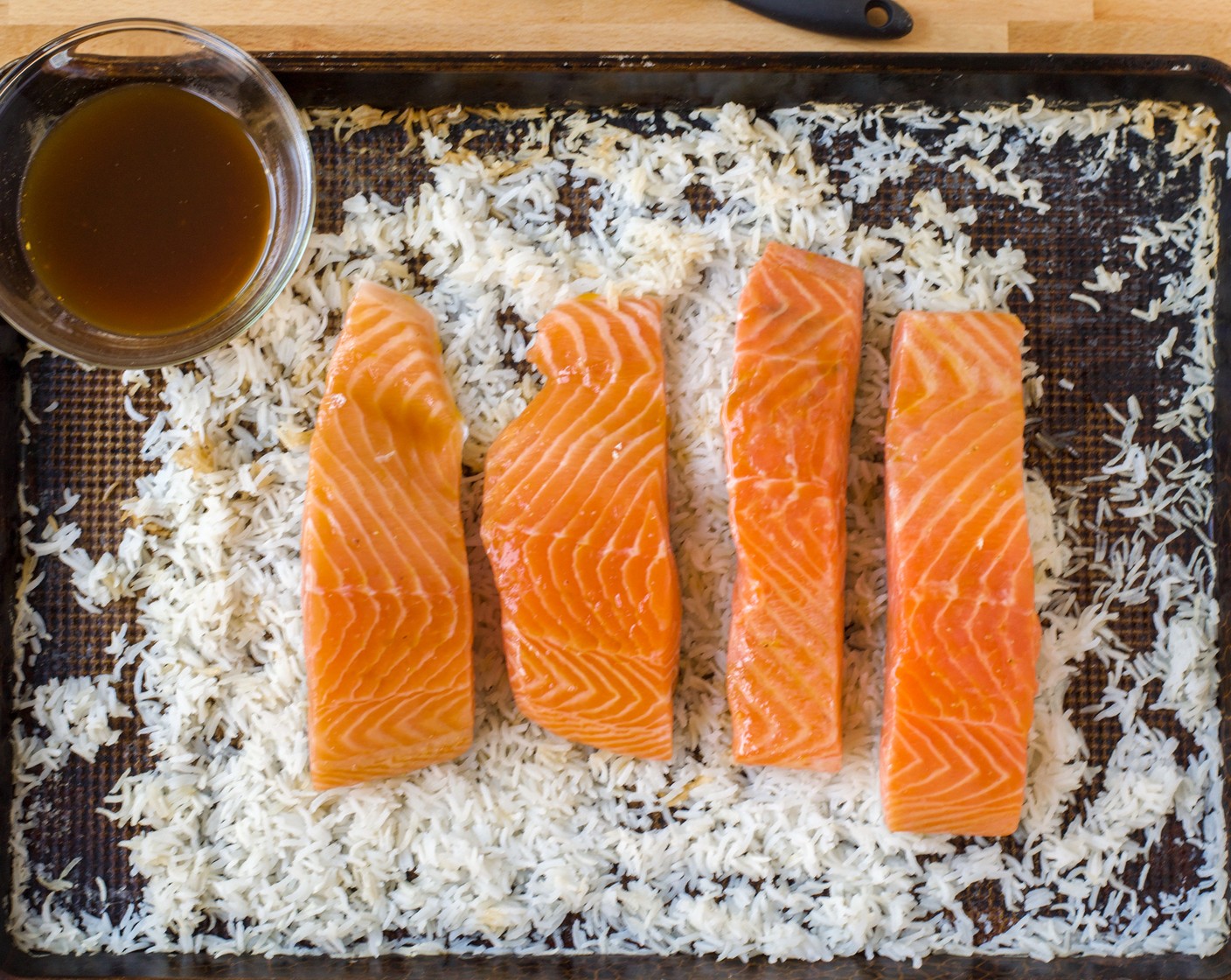 step 4 After the rice has cooked for 20 minutes, remove the sheet pan from the oven and place the Salmon Fillets (4) skin-side down on top of the rice. Brush the salmon with 1/3 of the glaze.