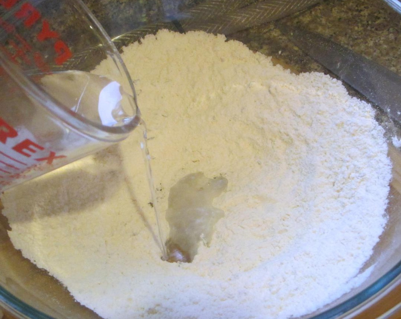 step 5 Make a well in the center, then add Water (1/4 cup) and Olive Oil (1 fl oz) and gradually stir into flour with a wooden spoon until a dough forms. Knead dough gently on a floured work surface 4 or 5 times.