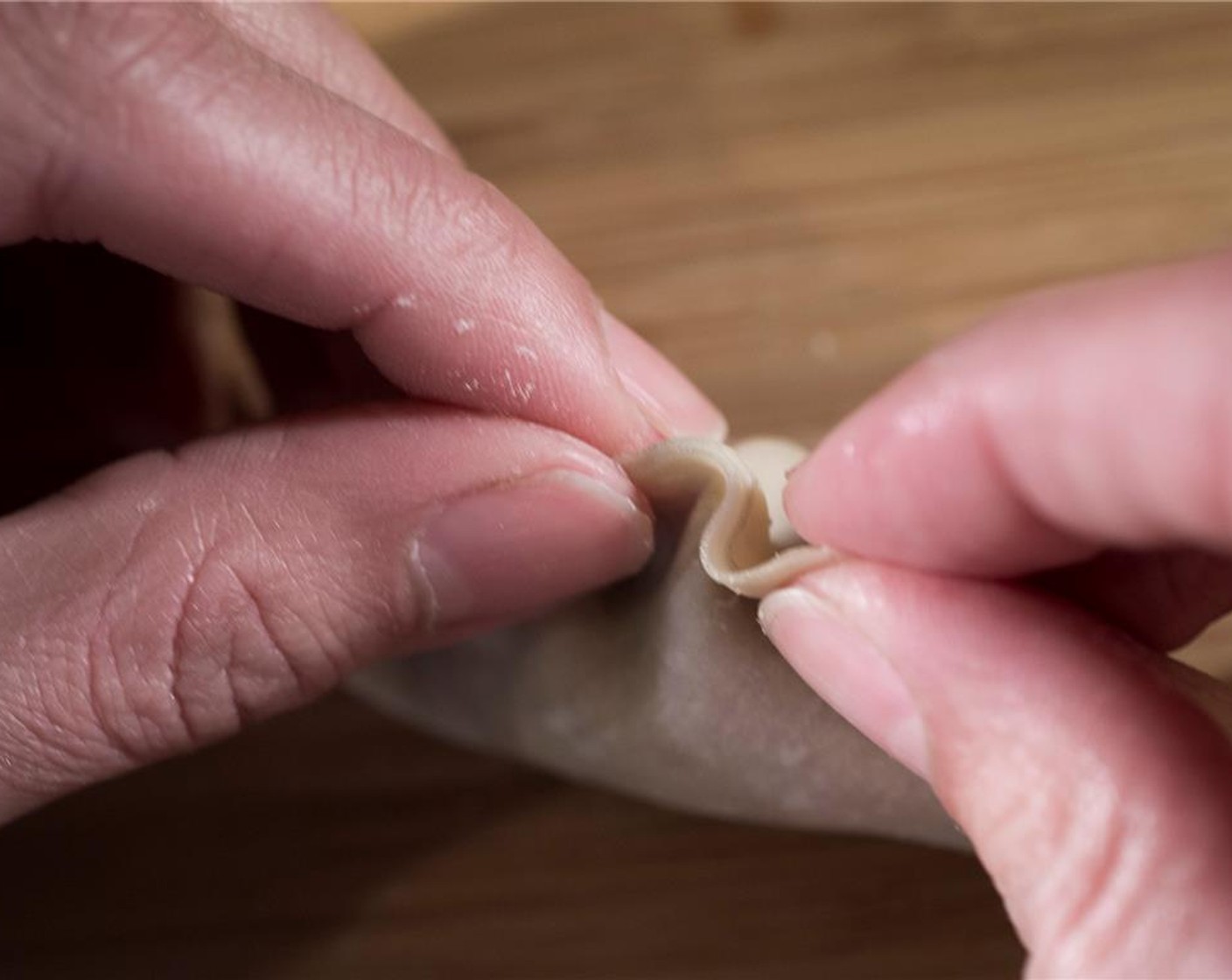 step 6 Fold the wrapper in half to form a crescent shape, gently pushing all the air out from around the pork mixture, so as not to leave any air bubbles. Starting at one end, create pleats all the way to the other end, gently pressing each pleat as you’re done to seal.