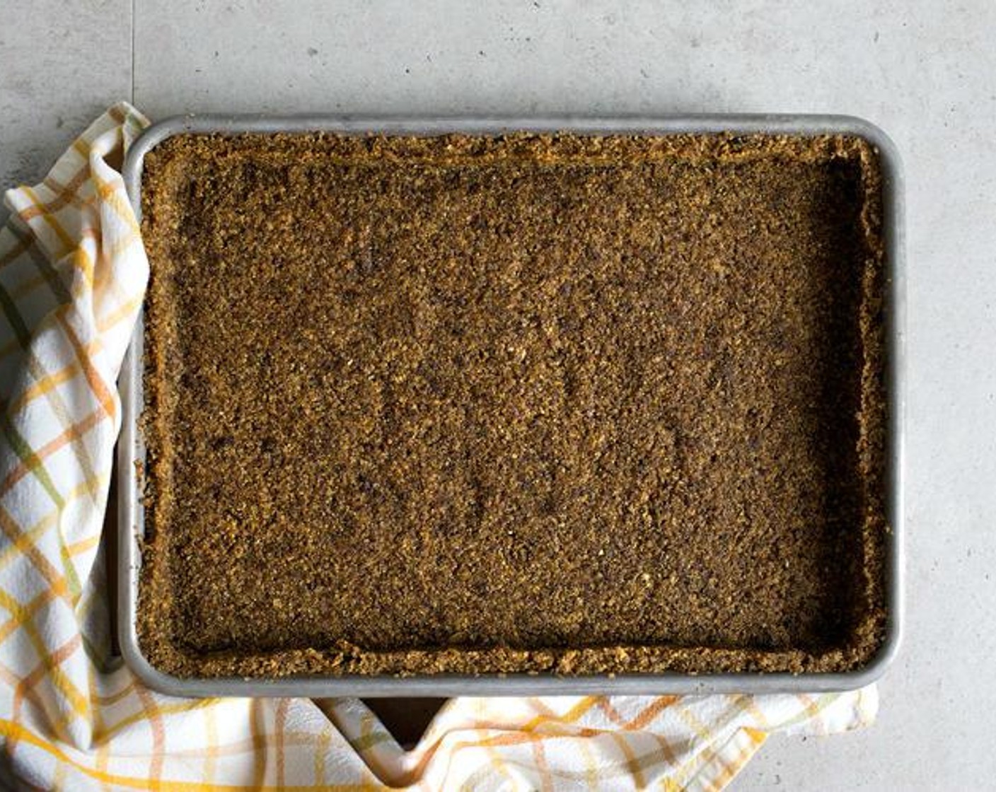 step 4 Transfer the mixture into a 8 1/2" x 12" (12 x 30 cm) pan, then spread and press it tightly with your fingers or a flat-bottomed cup, evenly on the bottom and the sides of the pan to make a crust.