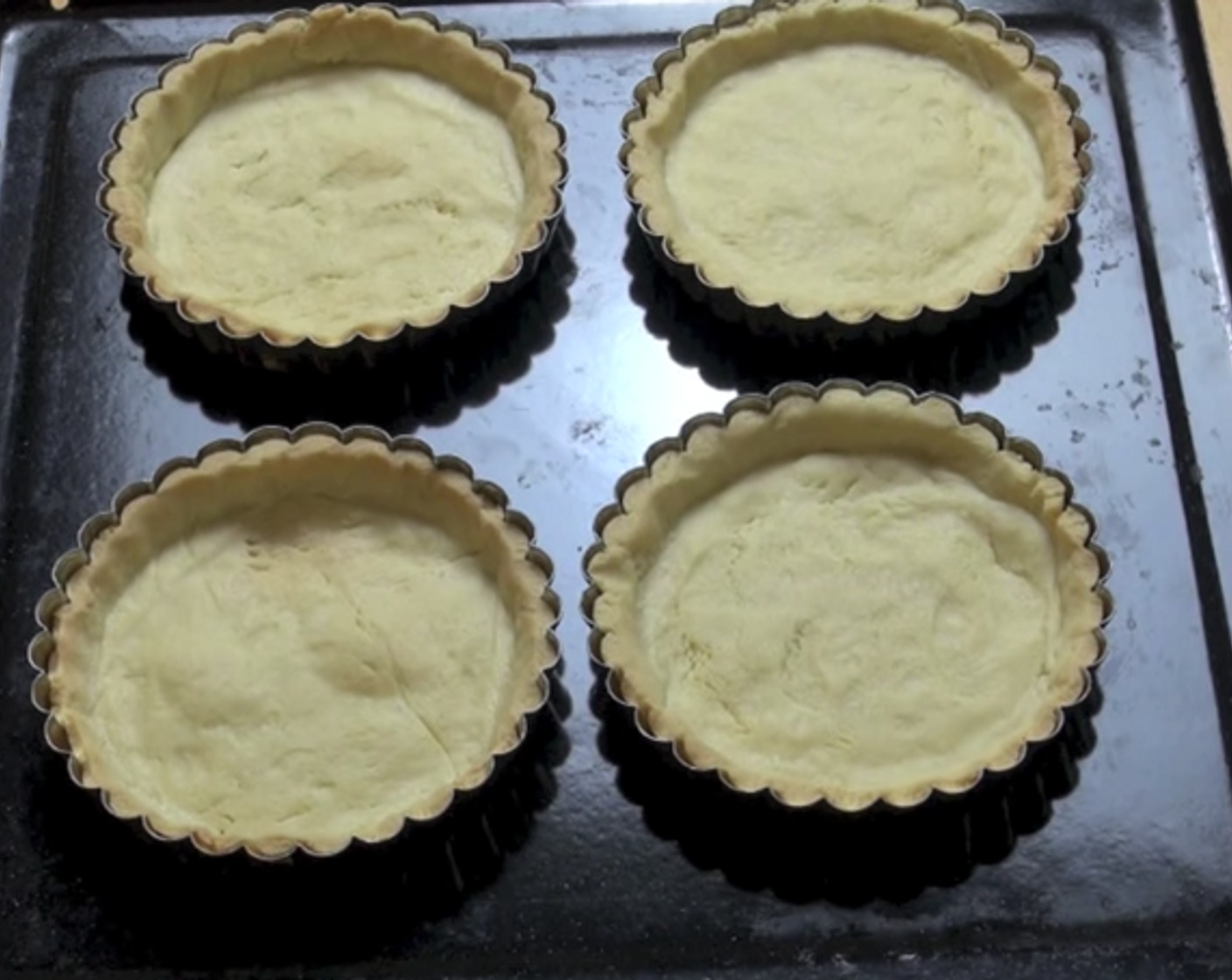 step 3 Using a rolling pin, flatten your dough until it is thin in thickness. Then, using your tart tins, cut out circular shapes from the dough, and press them into separate tart tins. Cover each tin with a baking paper, and bake under 180 degrees C (350 degrees F) for about 15 minutes.