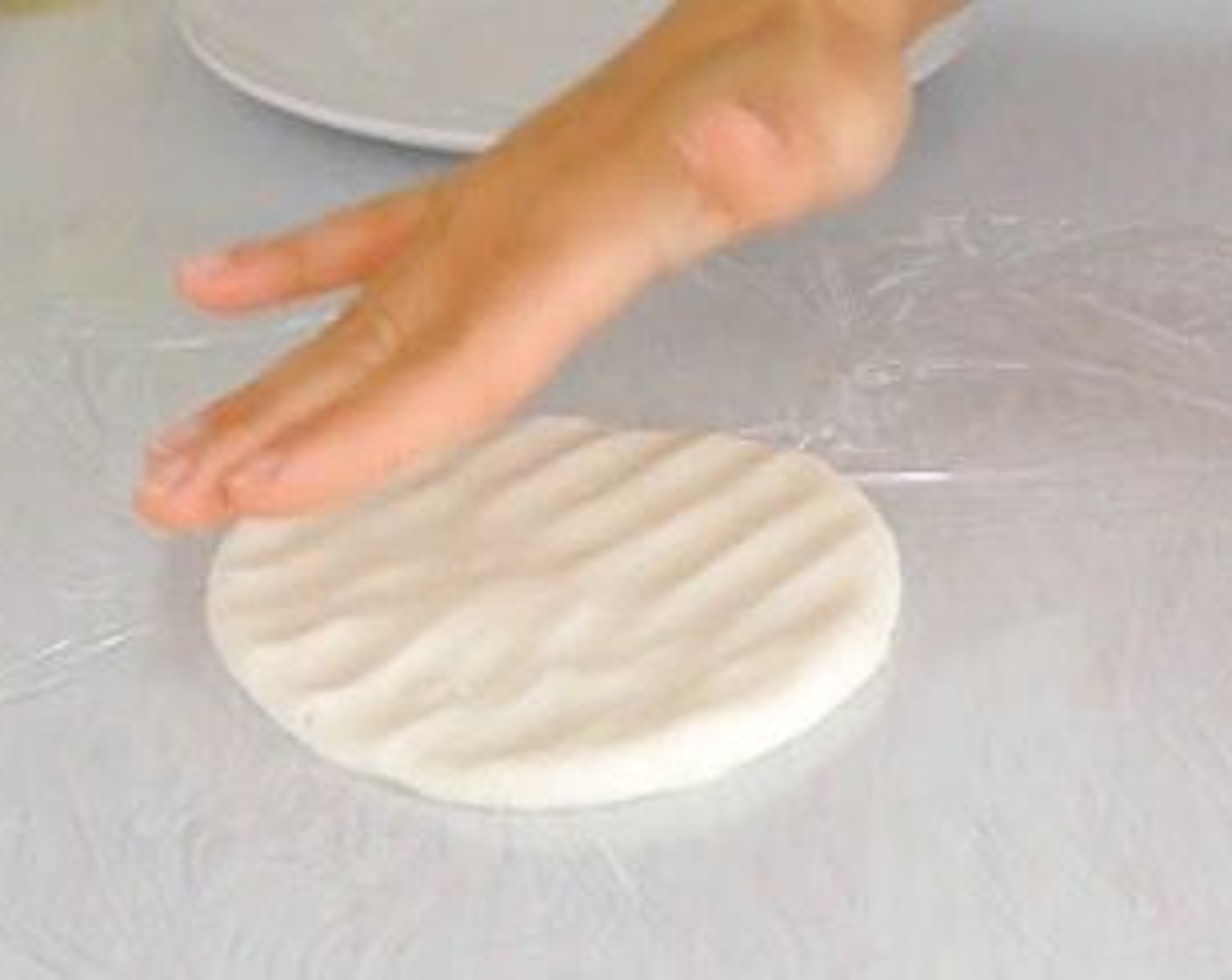 step 9 Then take a ball of dough, place it over the cling film and flatten it out until is 1/2cm thick. It helps to have a container with water to wet your fingers so the dough doesn’t stick.