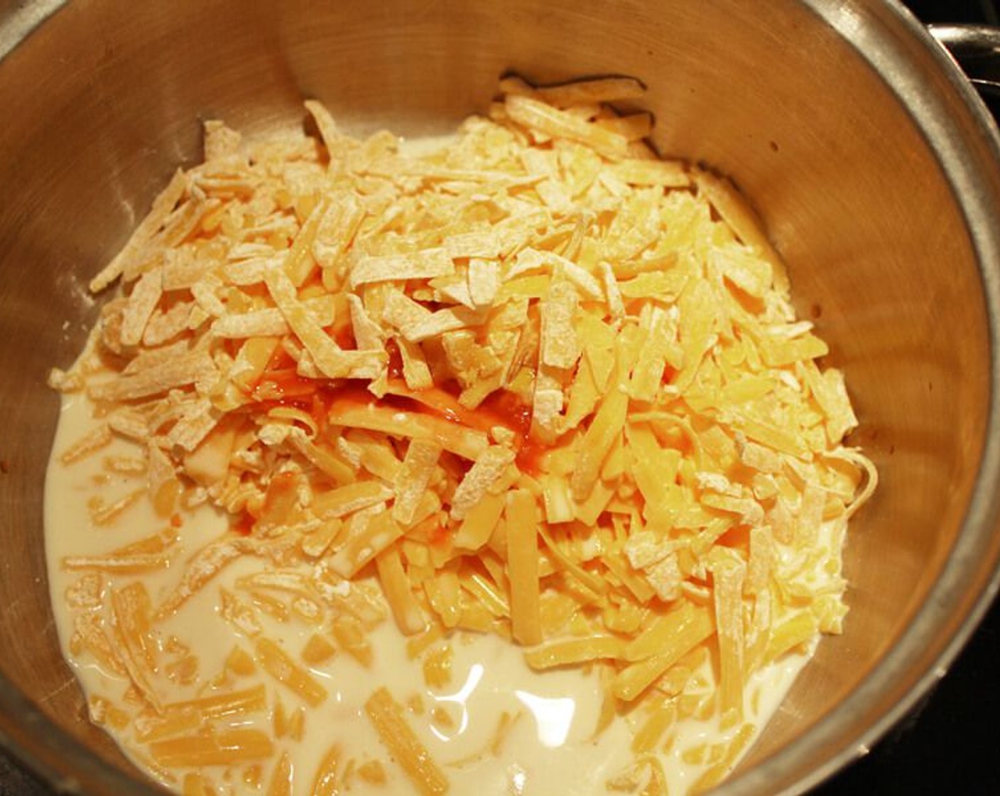 step 8 Now, make the cheesy sauce. In a medium sized bowl, toss Shredded Cheddar Cheese (2 cups) with Corn Starch (1 Tbsp). Toss until well coated. Transfer cheese mixture to medium sauce pan. Add Evaporated Milk (8 fl oz) and Hot Sauce (1/2 Tbsp). Cook over low heat, stirring constantly.