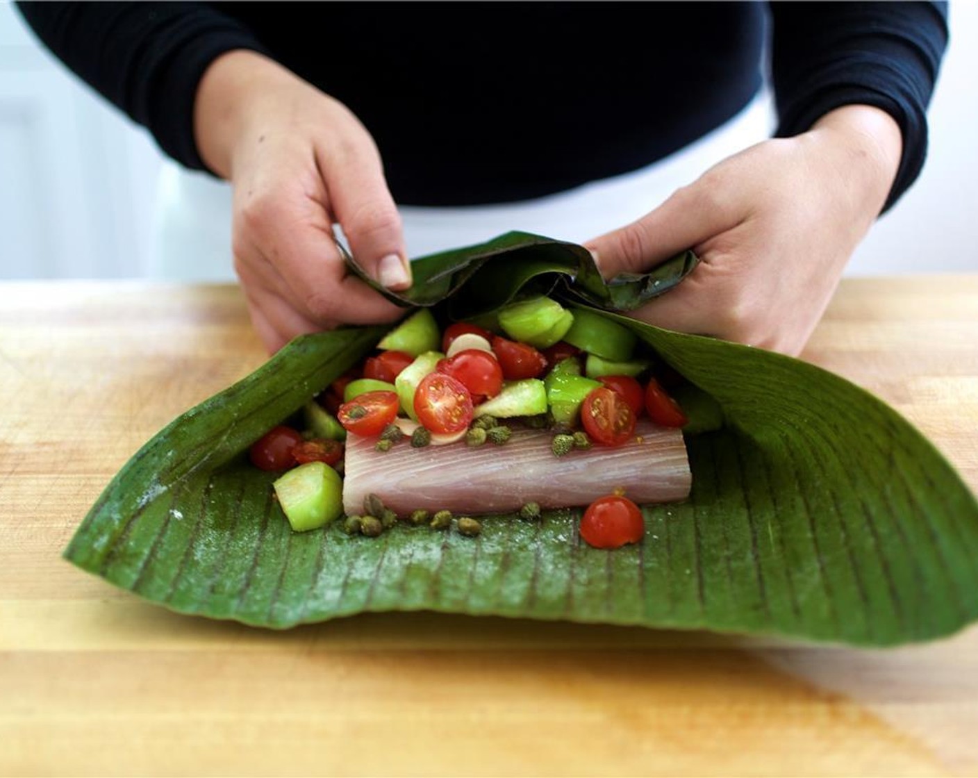 step 5 Scatter the tomatillos, tomatoes, sliced Garlic (2 cloves) and Capers (2 Tbsp) on top of the fish. Add the Bay Leaf (1) and half of the Fresh Thyme (3 1/2 Tbsp). Wrap the banana leaves around the fish, completely encasing it.