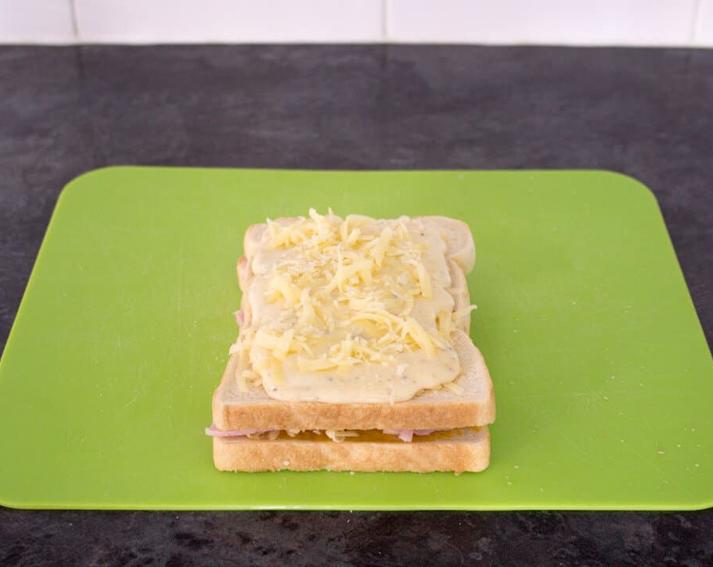 step 9 Next, place the bread with just cheddar cheese on top of the slice with ham on it.
Pour over the sauce and spread around evenly. Then top with the remaining cheddar cheese and place onto a baking tray.
