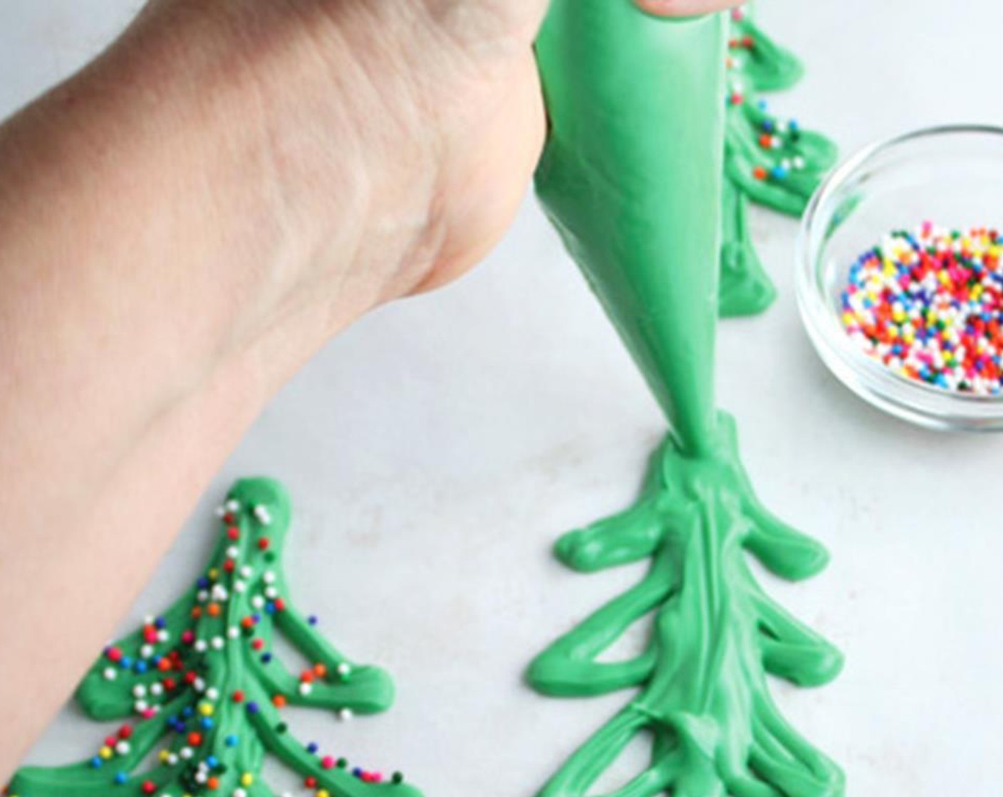 step 6 Cut a small corner off the pastry bag, then pipe your Christmas trees onto the parchment paper. They don't have to be perfect. Start with a thick line going up and down. Then go to the left and right, piping the branches of the tree. Add Sprinkles (to taste). Refrigerate for 30 minutes.