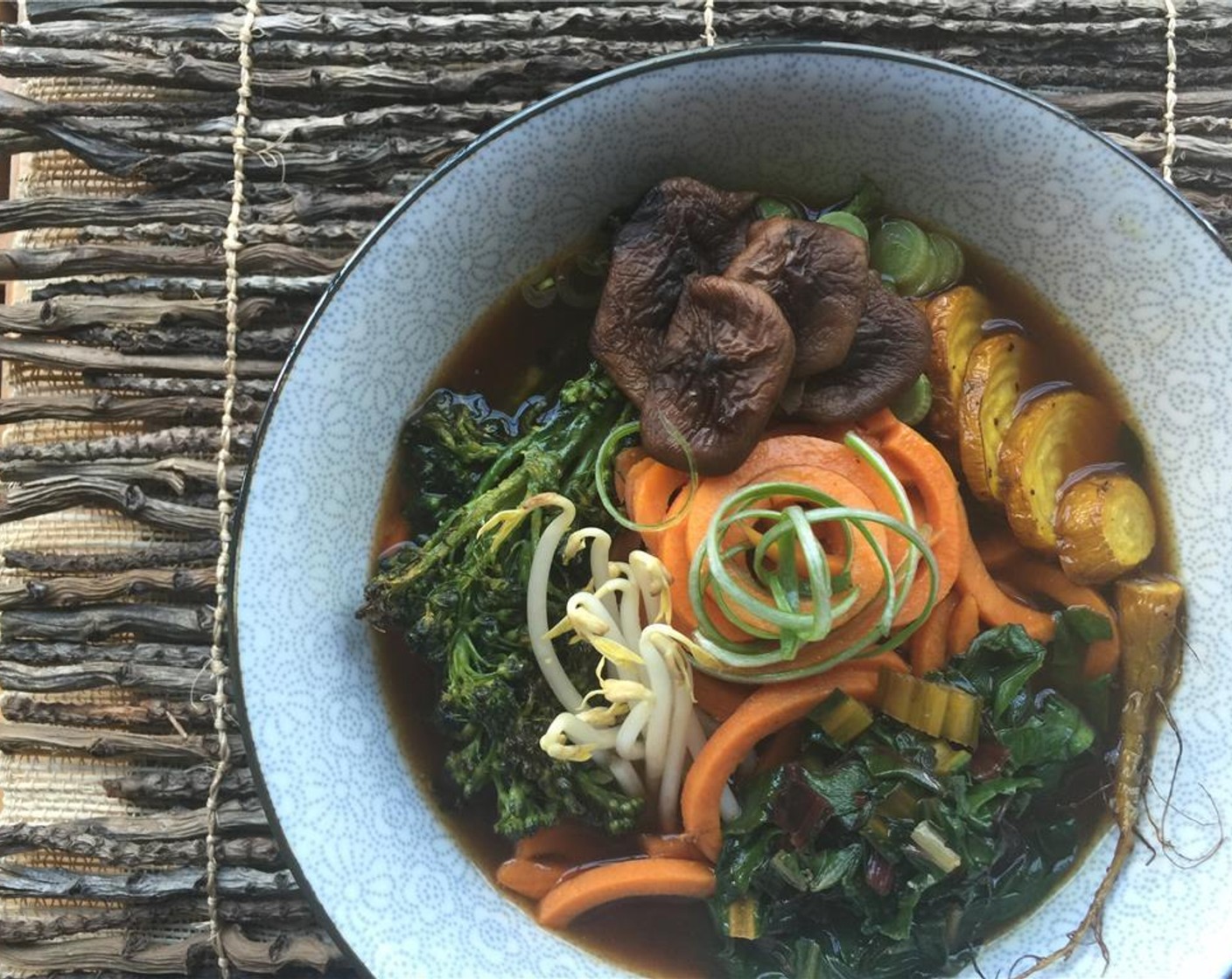 step 19 Stack the potato noodles high in bowls. Ladle in dashi. Garnish with shiitake mushrooms, sliced scallion, sautéed rainbow chard, bean sprouts, roasted broccolini and golden beets. Top with thinly sliced spring onions.