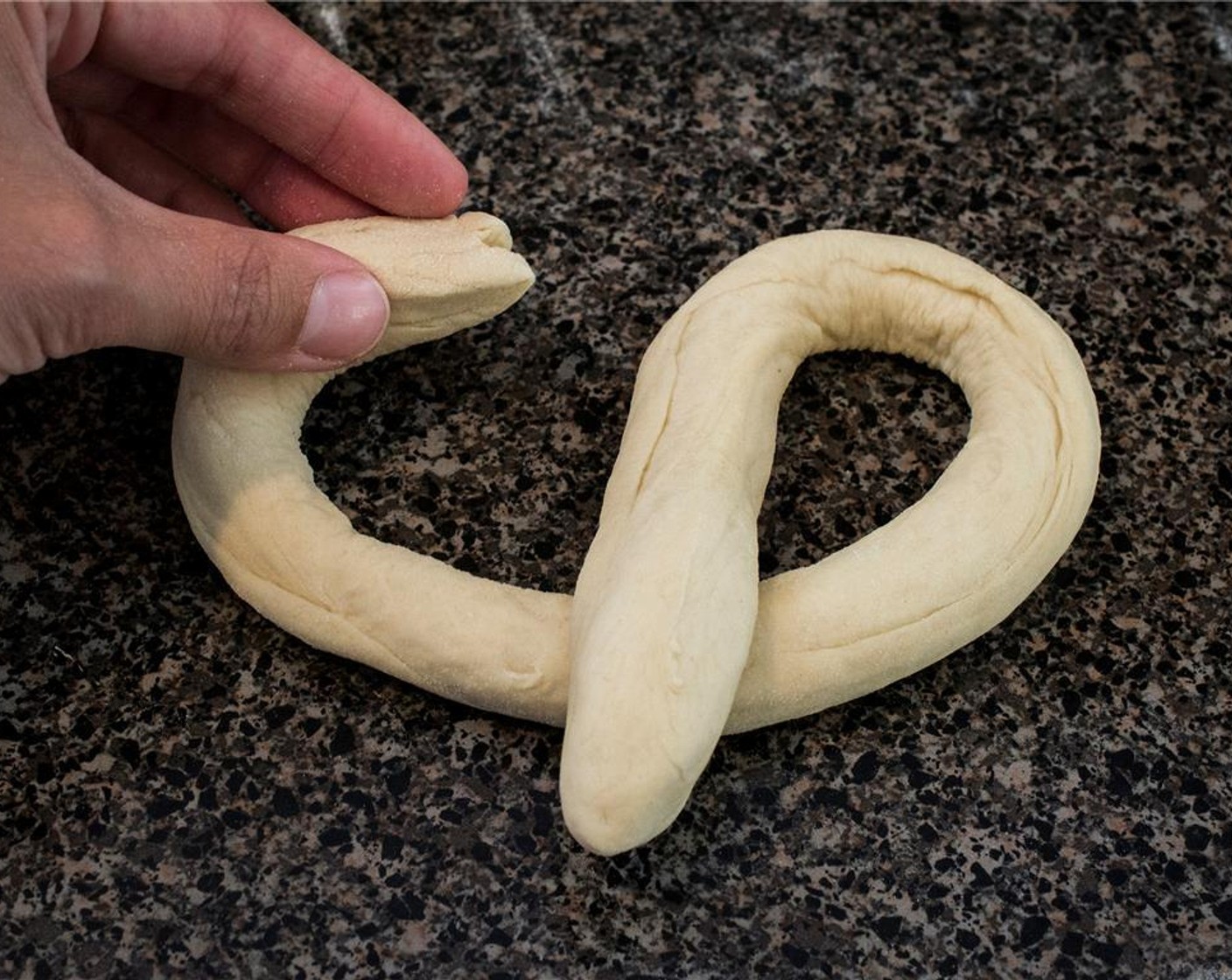 step 9 Take one ball of dough, roll it out into a 22-inch rope using your hands. Making a U-shape with the dough, cross the right side over to the left, and left over to the right. Gently press the ends into the bottom of the U.
