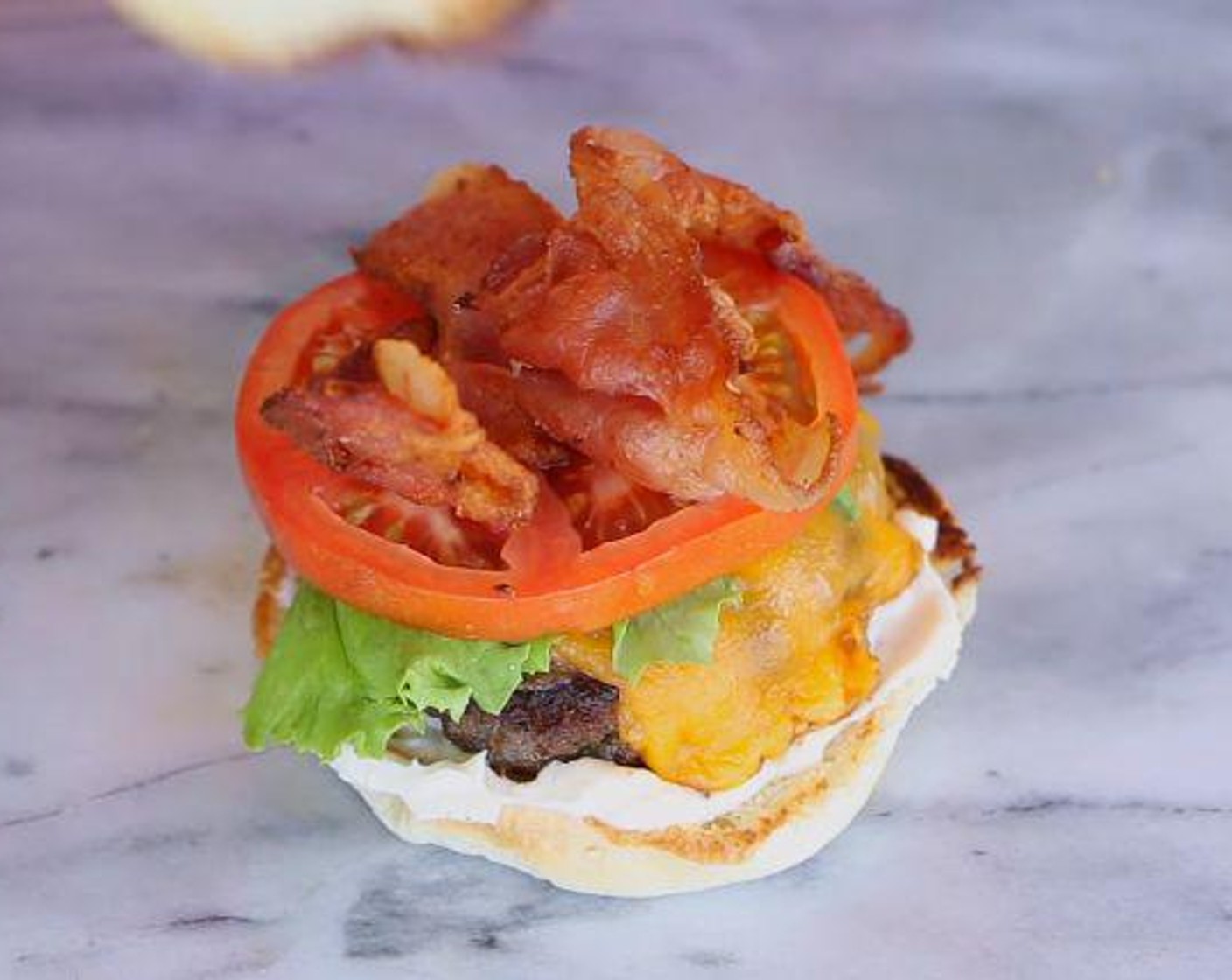 step 5 Toast the Hamburger Buns (4) in an oiled pan and begin assembling your burger. First, spread the Mayonnaise (to taste) on the buns, followed by the patty and melted cheese, some Lettuce Leaves (4), Tomato (1), and 2 slices of the bacon per sandwich.