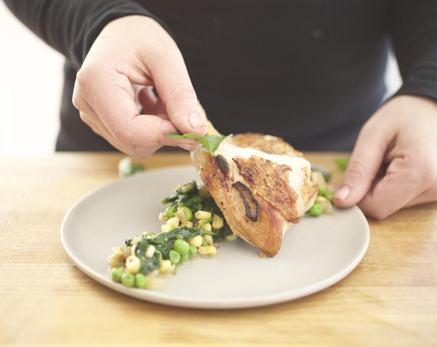 step 15 Slice the chicken in half on the bias. Arrange the spinach in a line down the center of two plates.  Spoon the succotash around the spinach, top with chicken. Drizzle the liquid from succotash around and on top of the plate. Garnish with the parsley leaves. Serve and enjoy!