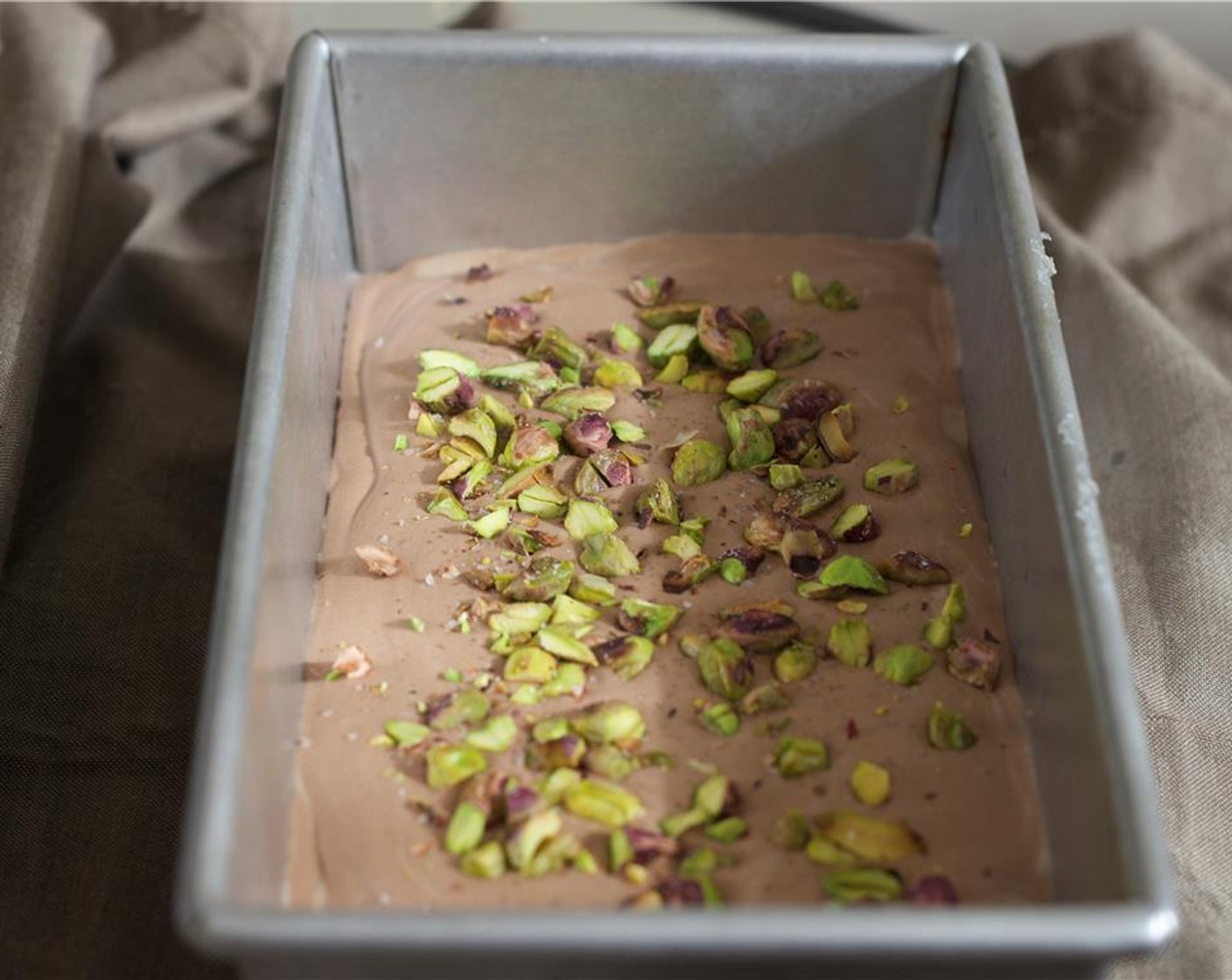 step 6 Pour the mixture into a loaf pan. Top with remaining pistachios. Cover with foil and place in the freezer for 6 hours.