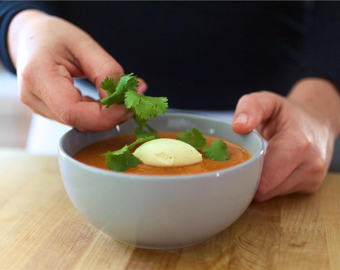 step 12 Ladle the soup evenly into two bowls. Place a dollop of the curried whipped cream in the center of the soup, and garnish with cilantro leaves.