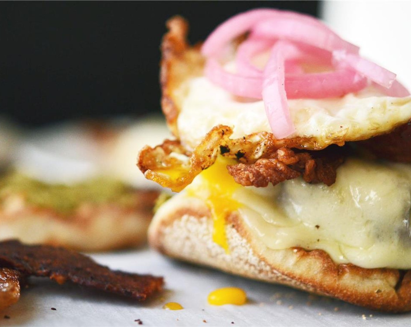 step 4 Atop the pesto on the bottom half of the English muffin, place the provolone covered hamburger patty, crispy bacon, fried egg, and Pickled Red Onions (to taste) on top.