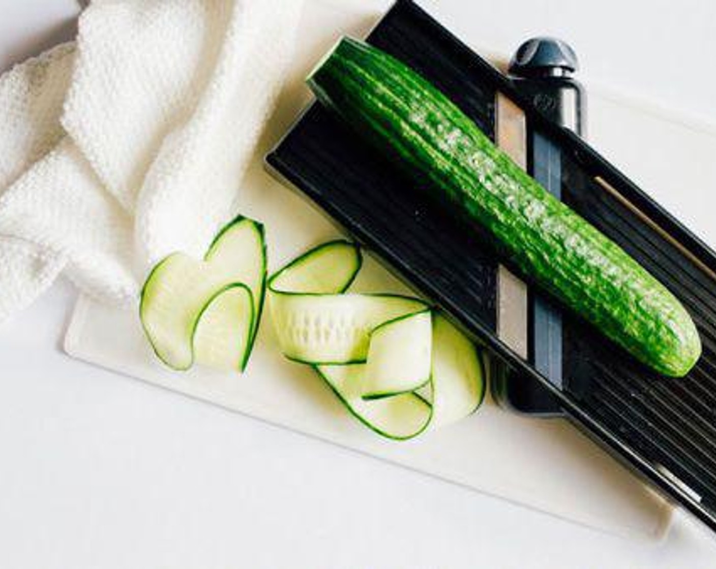 step 1 Chop the ends off of the Cucumber (1) and use a mandolin or vegetable peeler to peel thin slices along, lengthwise. Set slices on a few layers of paper towels and cover with a few more. Pat to dry and let sit while you make the tzatziki.