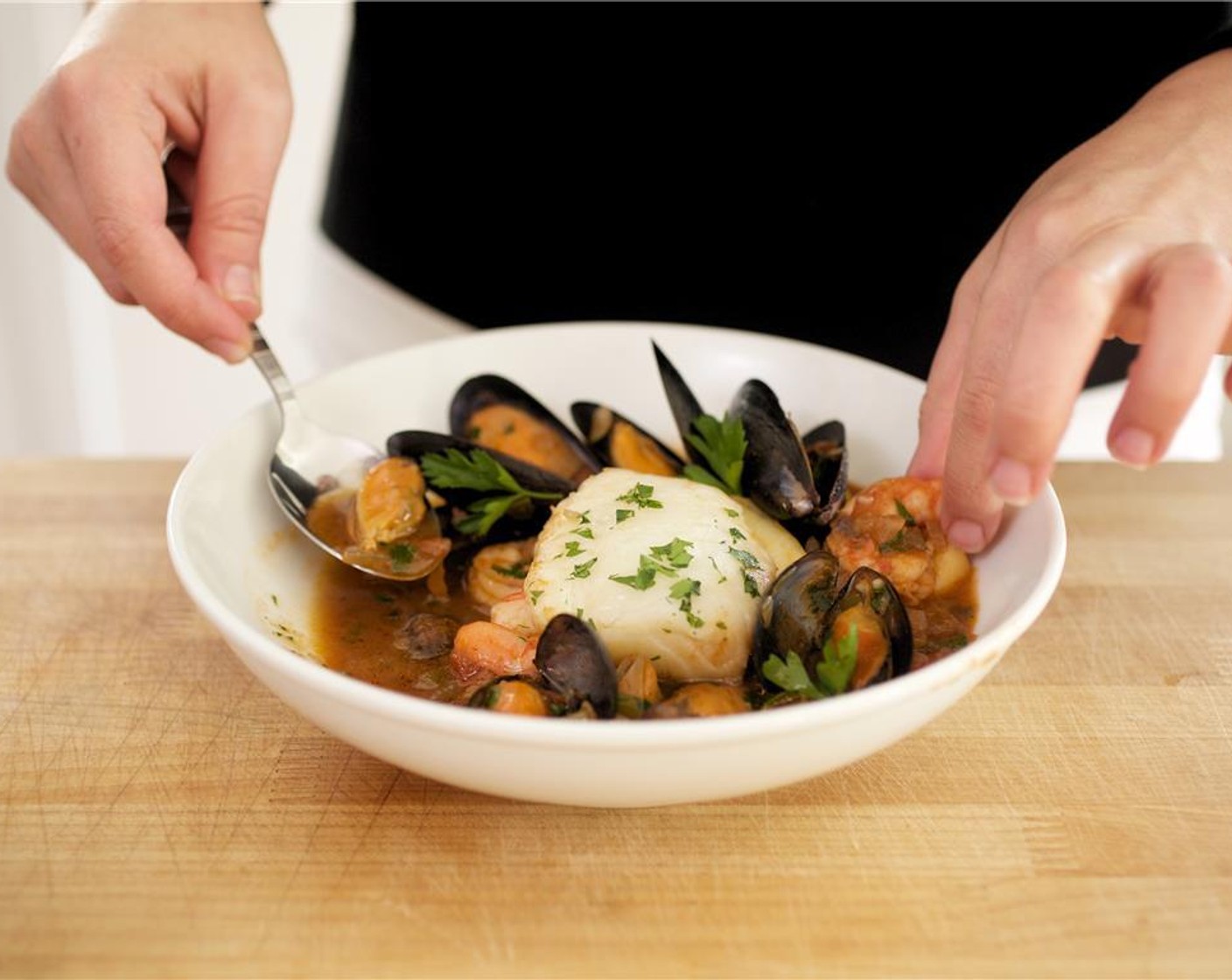 step 22 Remove the baguettes from the oven and cut in half on a bias. Place the cioppino into two bowls, making sure both bowls get plenty of seafood. Ladle the broth into each bowl. Garnish with the remaining parsley leaves. Serve the baguette on the side.