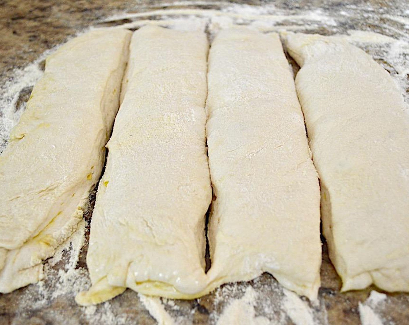 step 6 Turn the dough out gently onto the work surface gently, without deflating it or making it lose its shape. Dust more flour and semolina on the top. Cut it lengthwise into 4 equal loaves, then stretch each of them out just a bit to be a little longer.