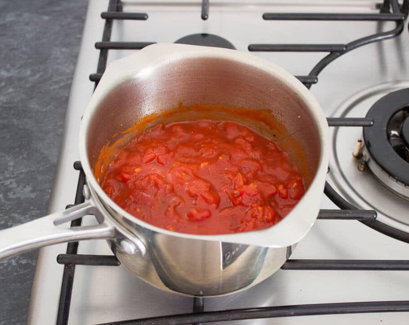step 2 Over medium heat, fry the Garlic (1 clove) in a little Olive Oil (1/2 Tbsp) in a heavy-bottomed saucepan for a minute then add the Canned Chopped Tomatoes (2 cups).
