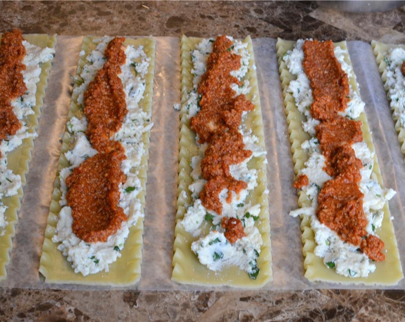 step 10 To assemble the lasagna rolls, lay the sheets out on parchment or wax paper. Spread the ricotta cheese mix along the sheets, then spoon some of the meat mix on each sheet as well.