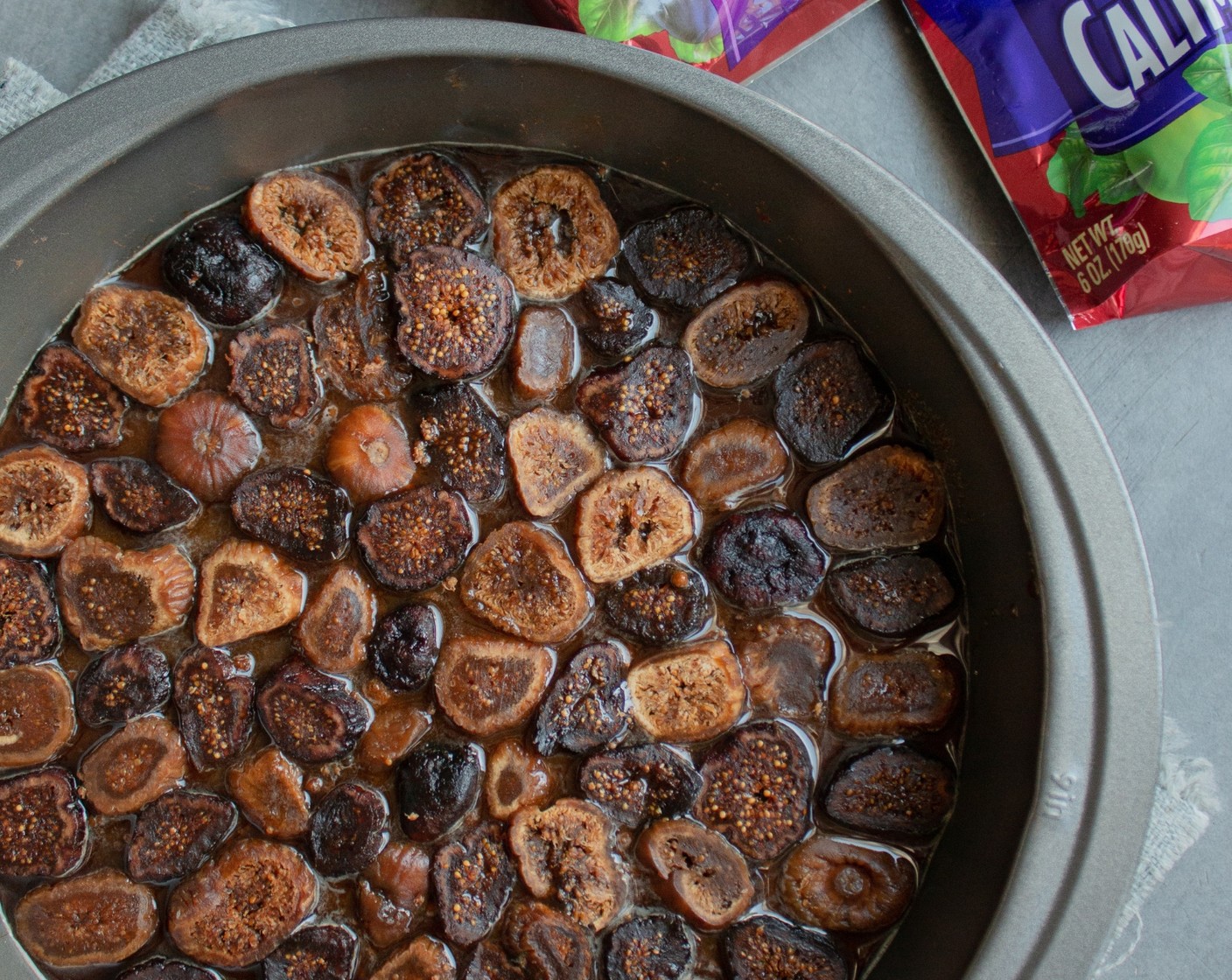 step 2 In a small bowl, mix Water (2 Tbsp), Jaggery Powder (3 Tbsp), and Brown Sugar (1/4 cup) until you have a slurry. Pour the mixture into the bottom of the cake pan and spread evenly. Top with Dried Figs (12).