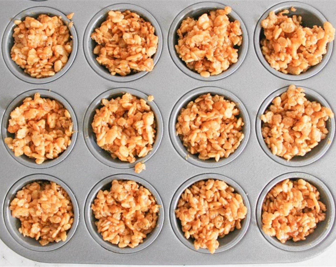 step 3 Grease a spoon with butter or cooking spray, and spoon the Rice Krispie mixture into the wells of the prepared mini muffin tin.