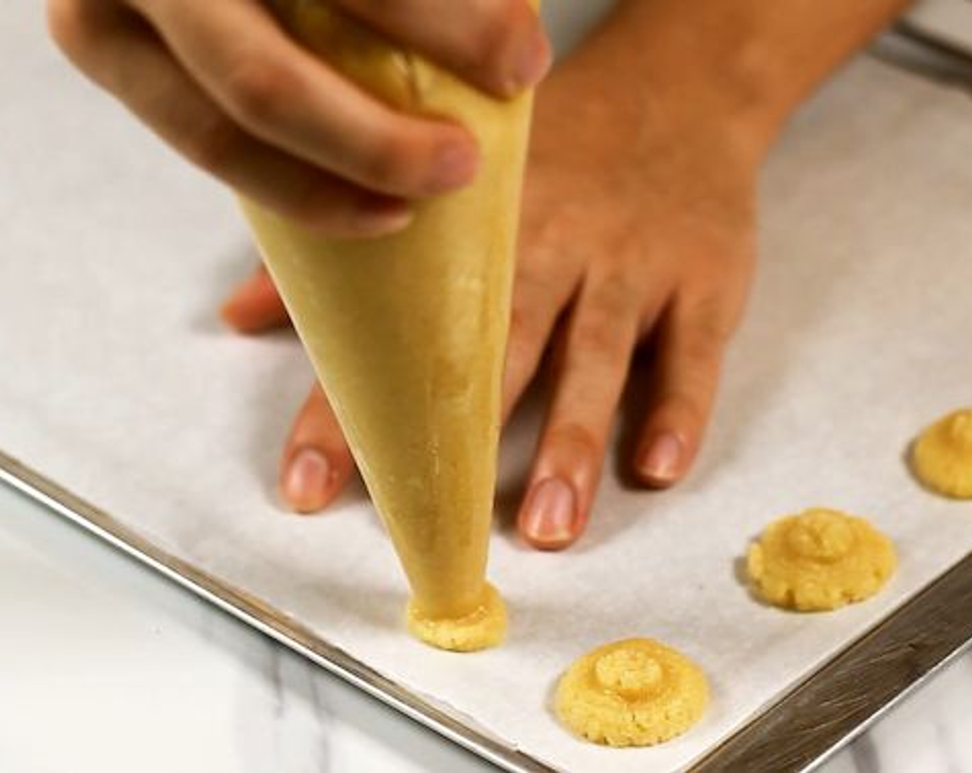 step 6 Pipe out a small coin worth of batter on a baking tray lined with parchment paper. Make sure to leave 2 fingers spacing as it will spread.