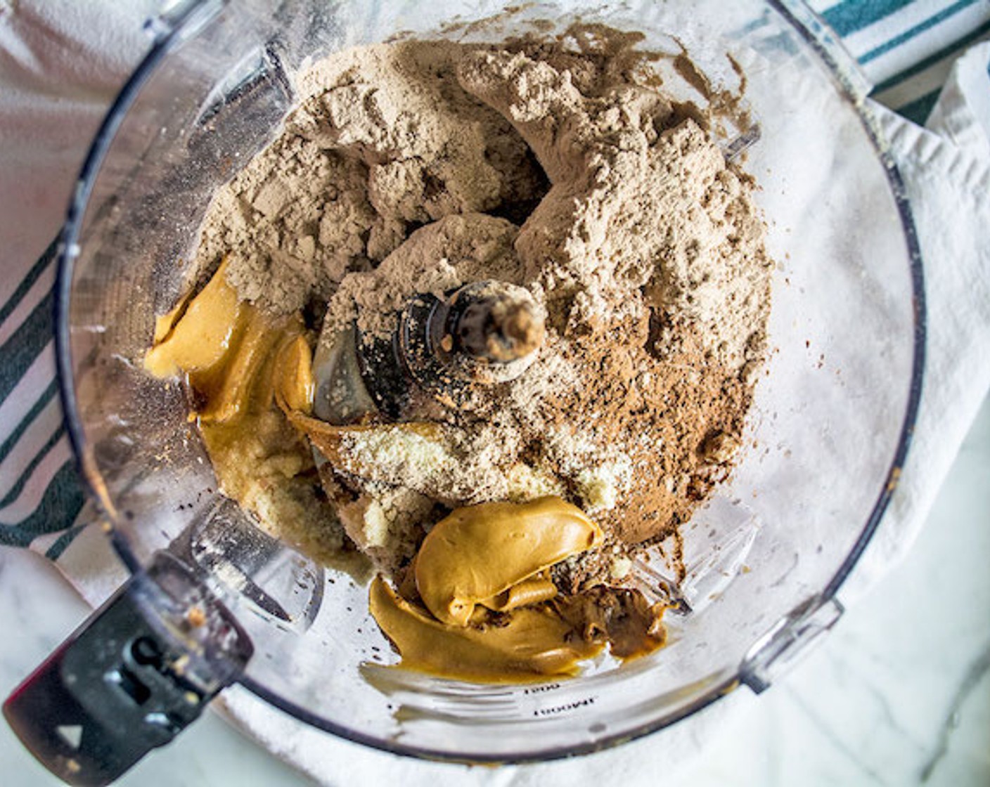 step 2 Add Almond Butter (1/2 cup), Medjool Dates (1 cup), Cacao Powder (1/2 cup), Chocolate Protein Powder (2 scoops), Maple Syrup (3 Tbsp), Almond Meal (2 Tbsp), and Water (2 Tbsp) to a bowl of the food processor.