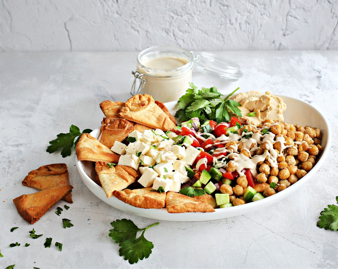 step 7 To assemble, place the baked pita chips on a platter and top with the roasted chickpeas, Seedless Cucumber (1), Cherry Tomatoes (2 cups), Red Onion (1/2), Feta Cheese (3/4 cup), and dollops of the Hummus (1 cup). Drizzle with the tahini sauce and serve extra on the side.
